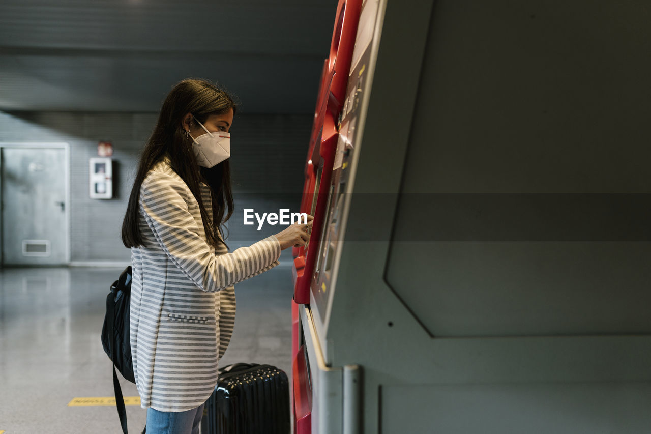 Woman with face mask using kiosk for buying train ticket during covid-19