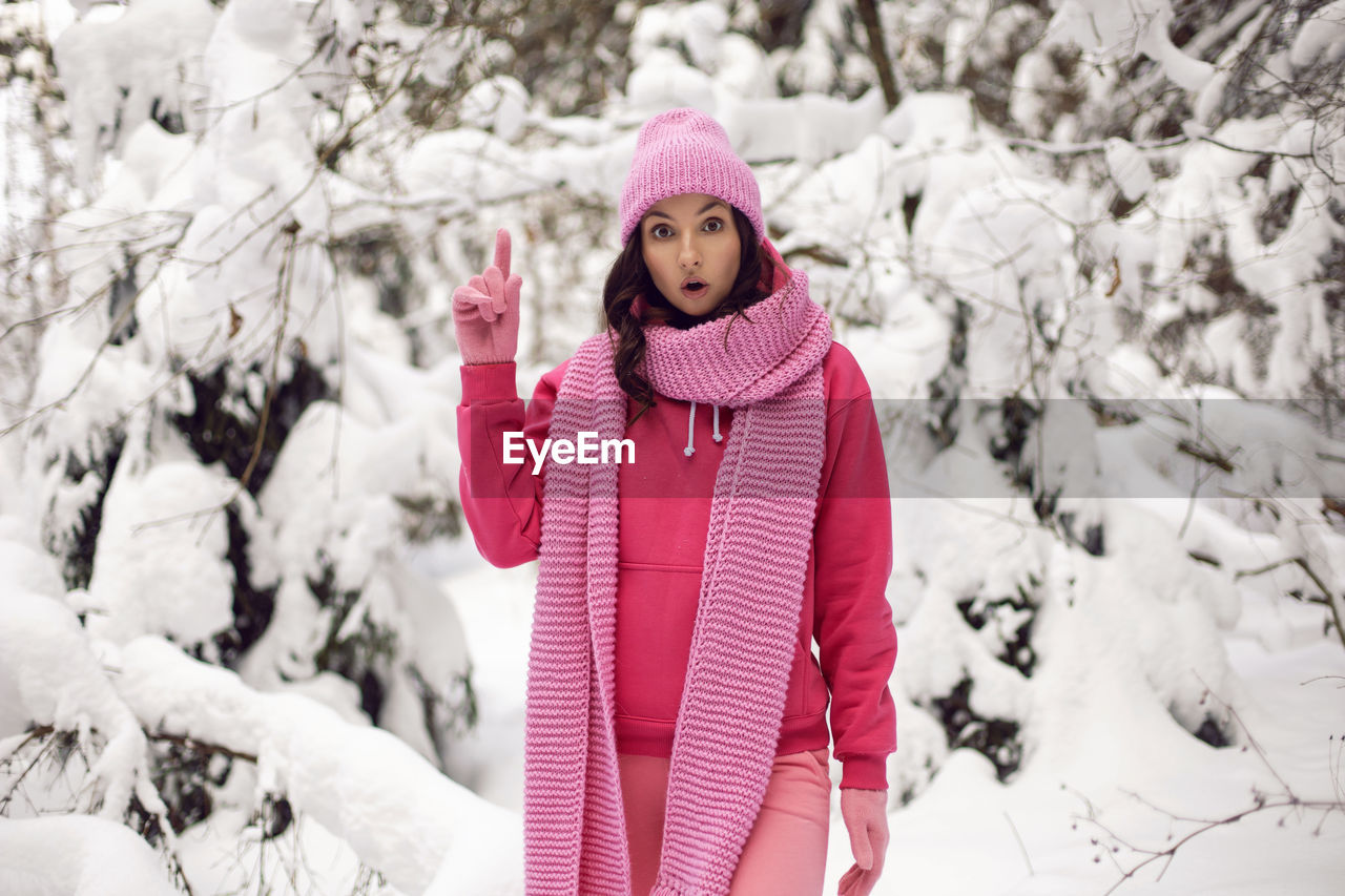 Woman thumbs up idea enjoy in pink clothes a jacket  knitted scarf hat stands snowy forest in winter