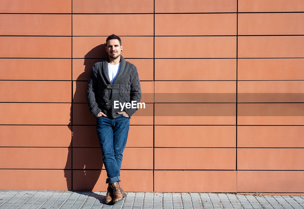 Front view of a fashionable young man standing against orange wall