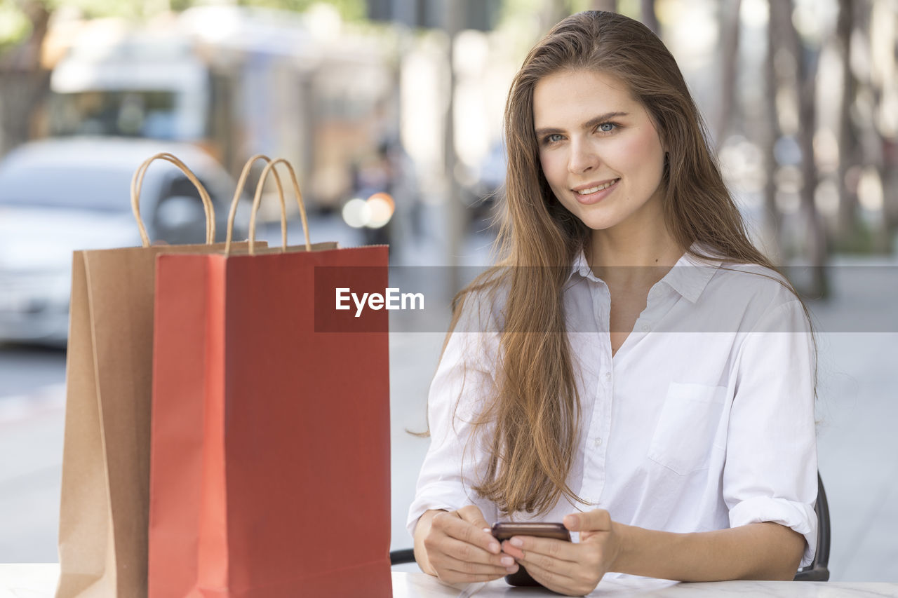 Portrait of young woman with shopping bags sitting outdoors