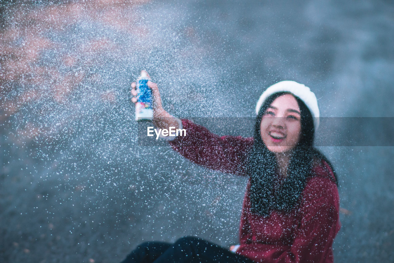 High angle close-up of smiling young woman spraying in snow