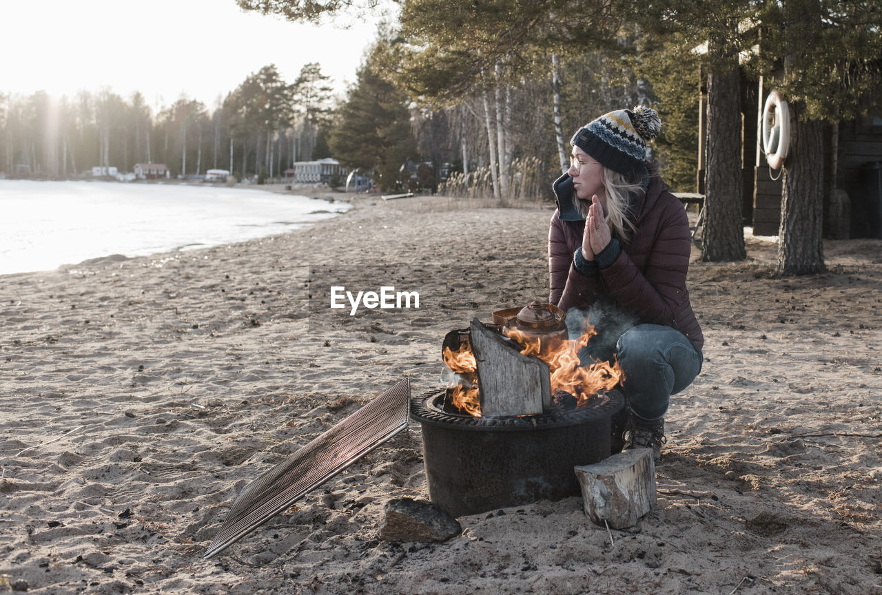 Woman warming up by a camp fire on a beach in winter in sweden