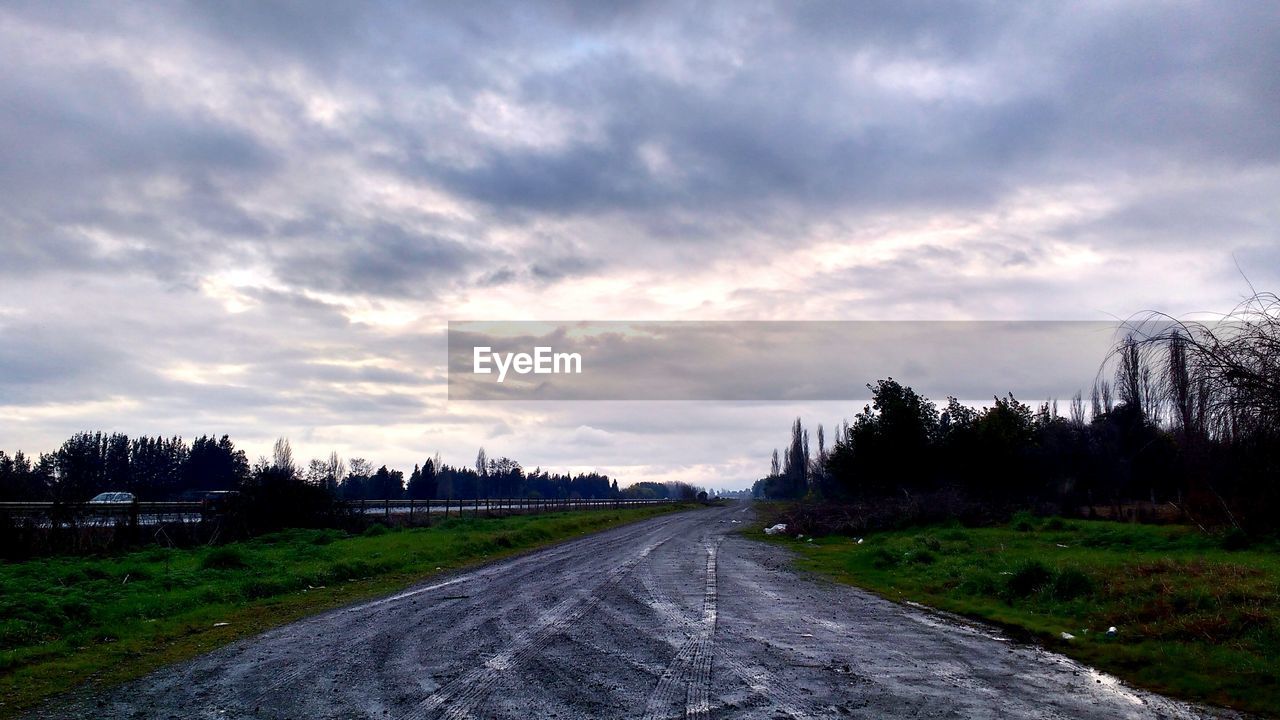 ROAD PASSING THROUGH FIELD AGAINST CLOUDY SKY