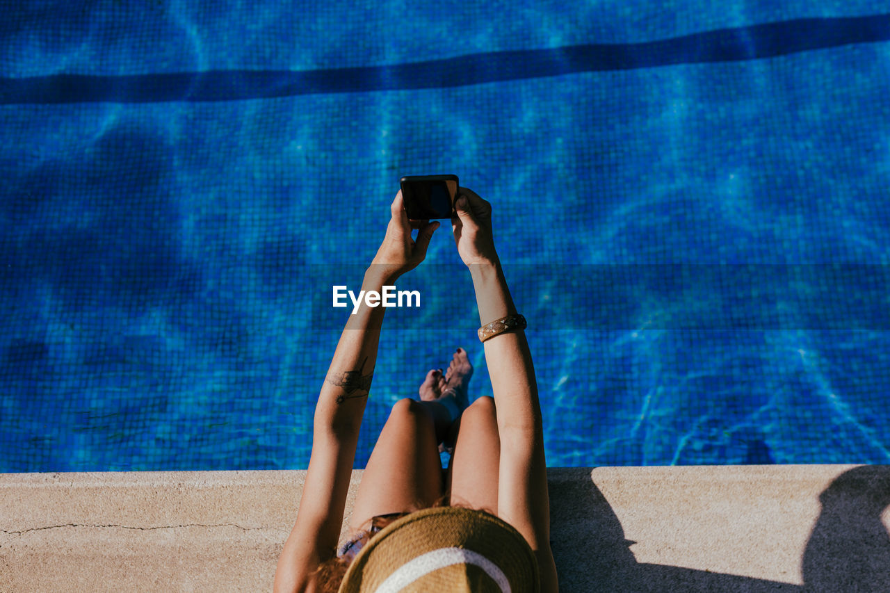 Low section of woman using smart phone at swimming pool