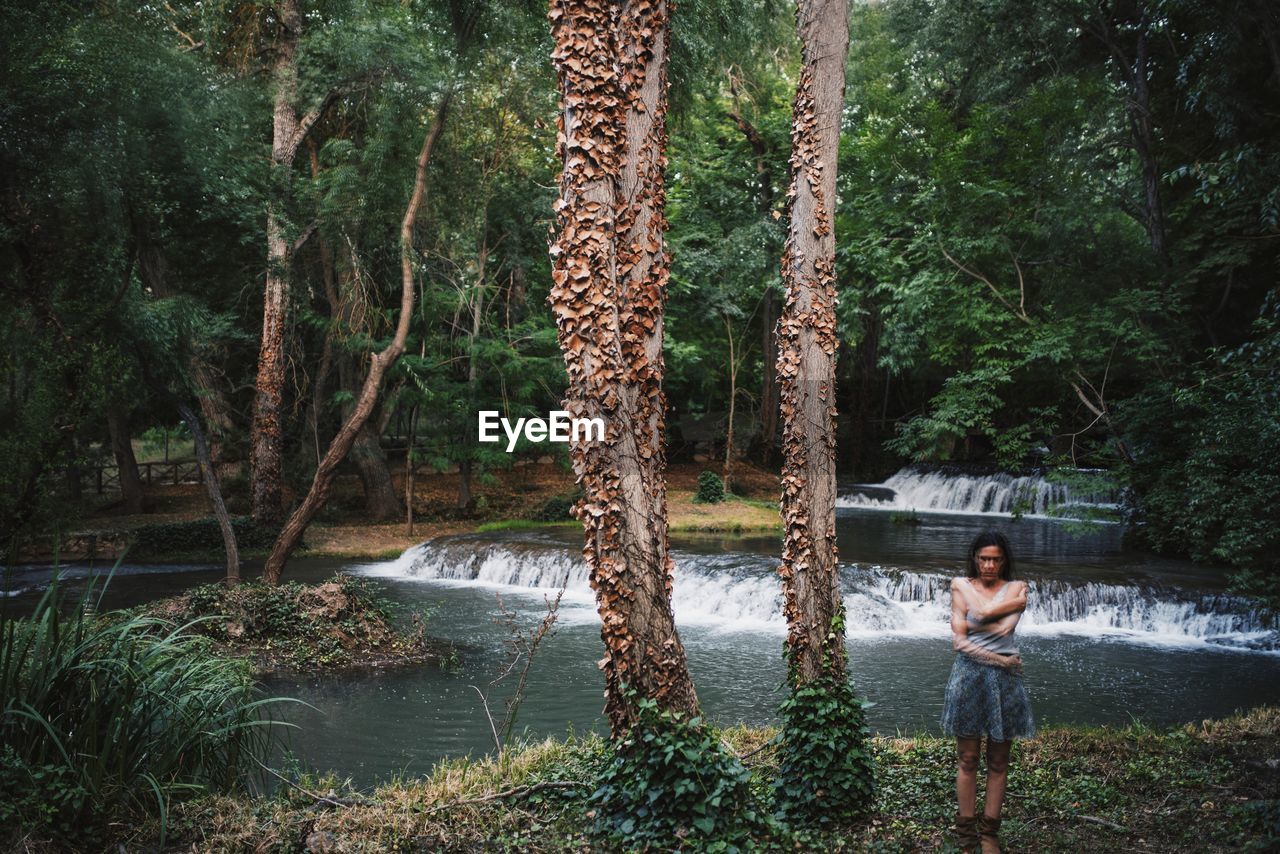 Multiple exposure of woman standing by tree in forest against river