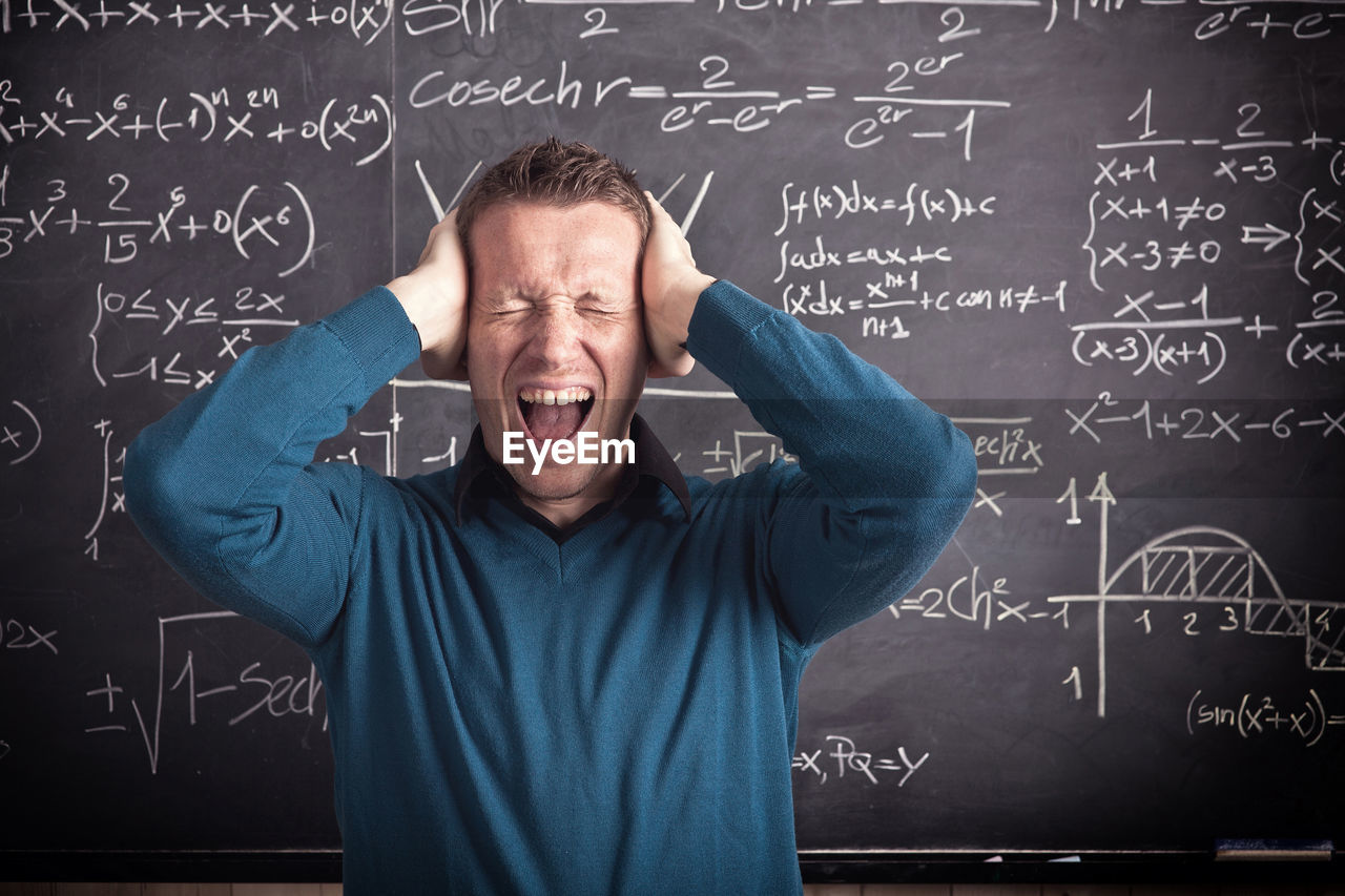 Frustrated teacher screaming against blackboard in classroom