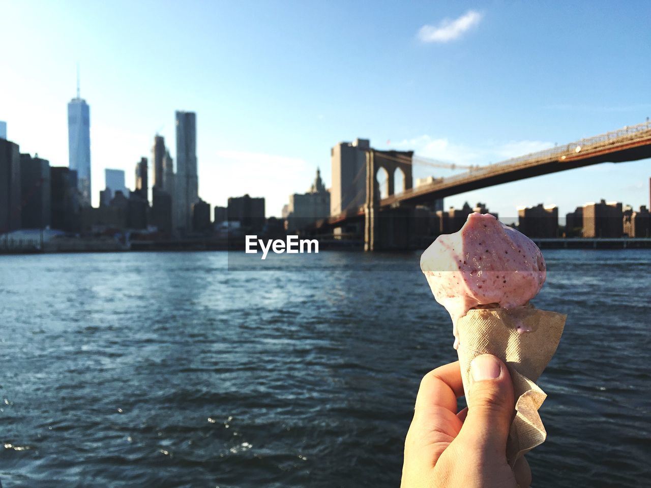 Cropped image of hand holding ice cream against brooklyn bridge