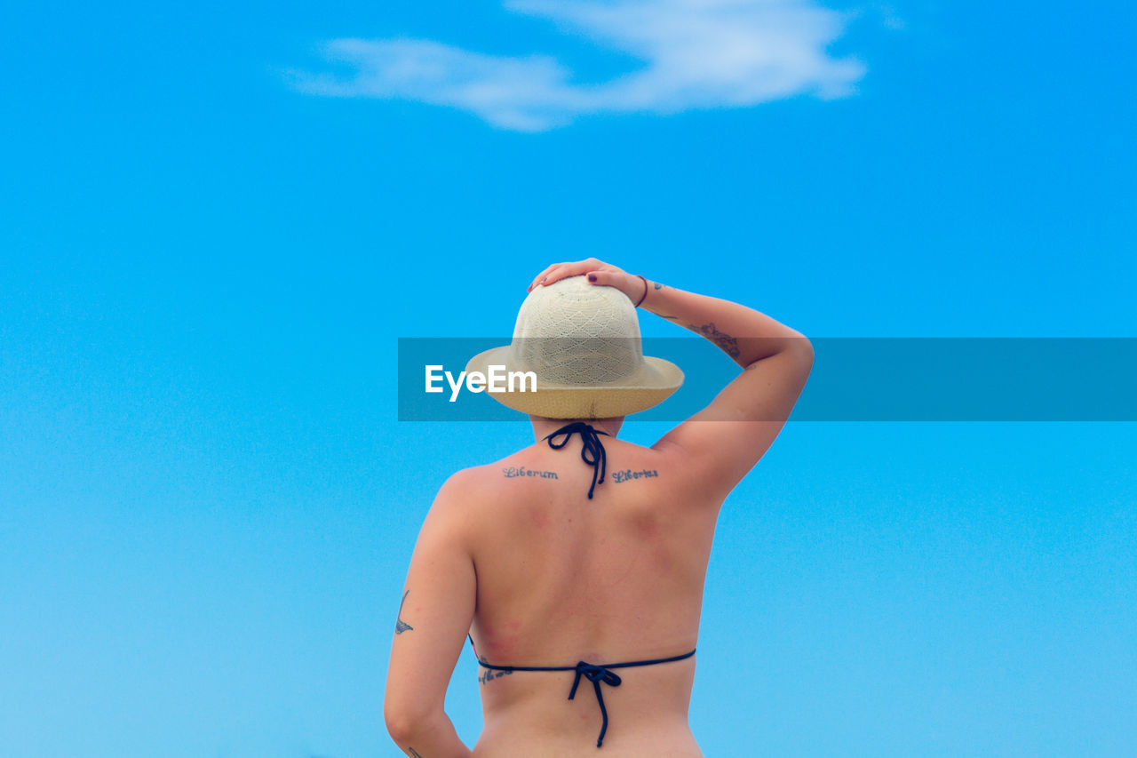 Rear view of bikini woman wearing hat against blue sky