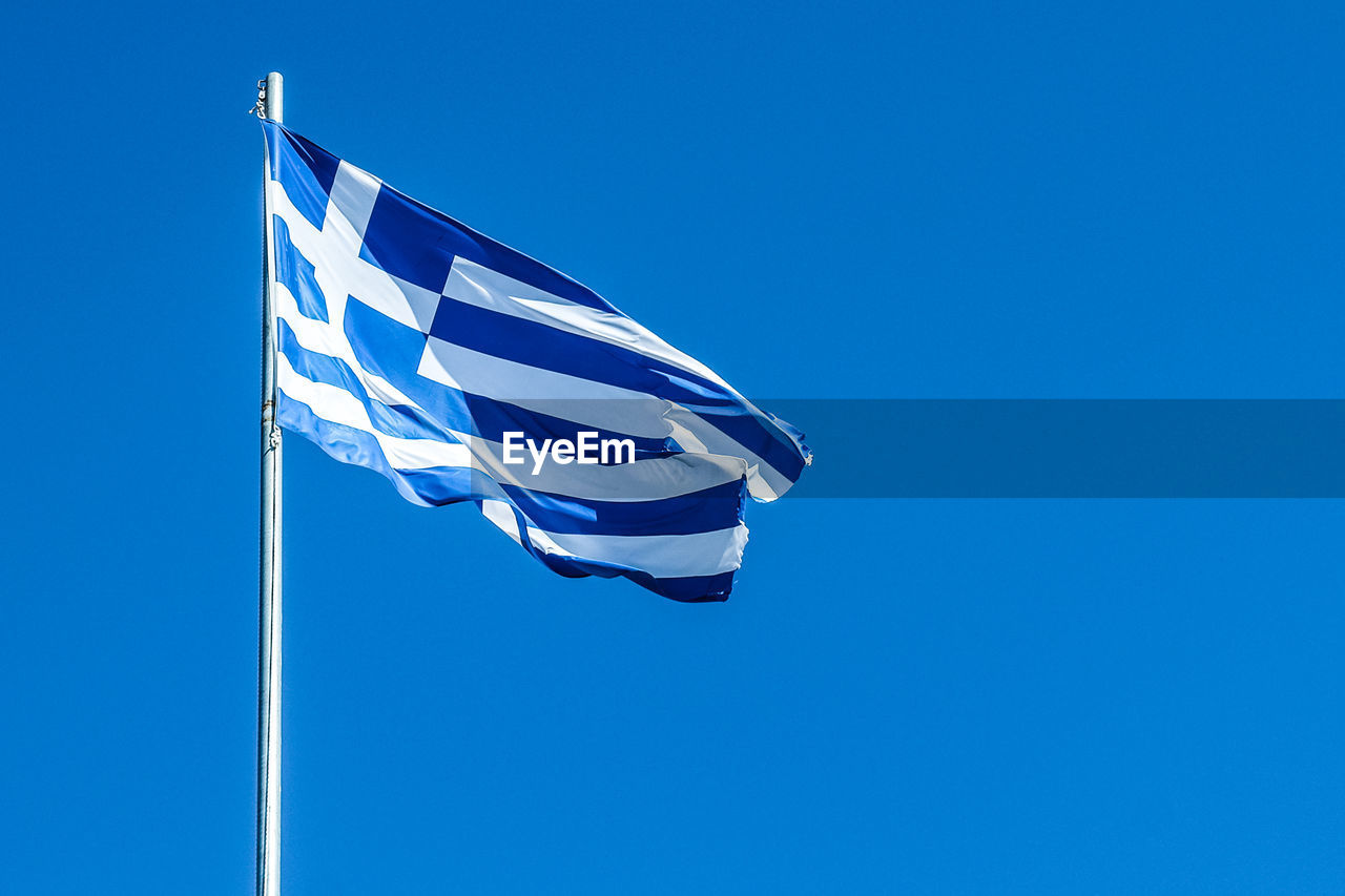Low angle view of greek flag against clear blue sky