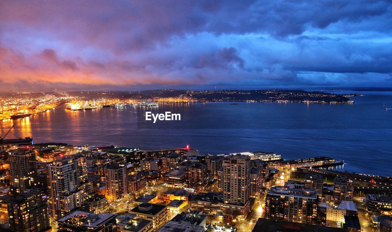 High angle view of illuminated city by sea against sky