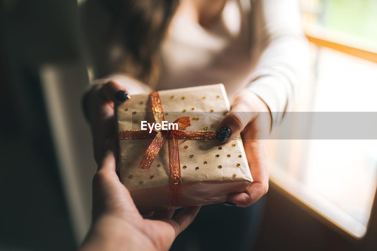 Young women with black glitter nails giving a christmas present box to his friend. 