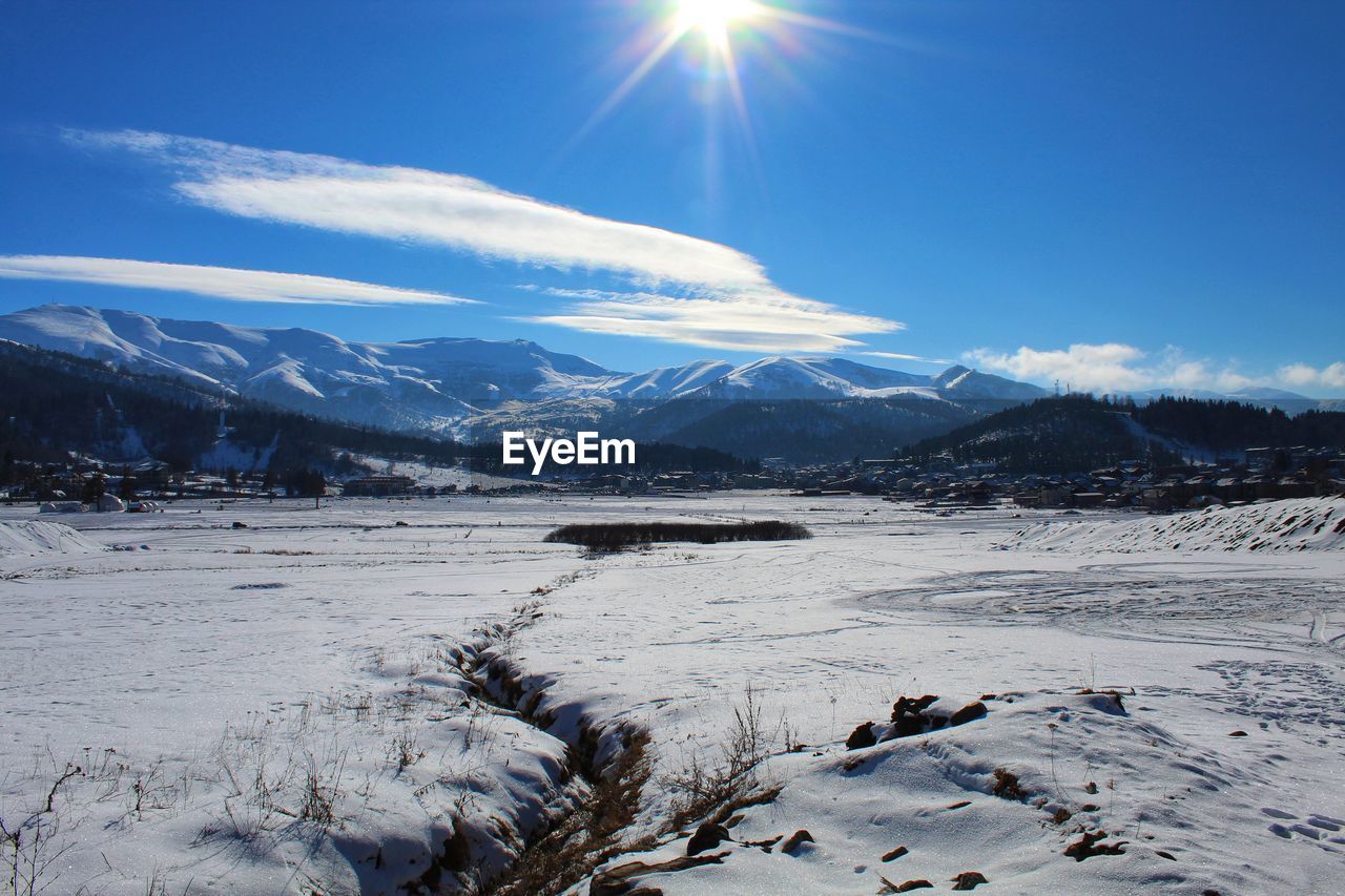 Scenic view of snow covered mountains against bright sun