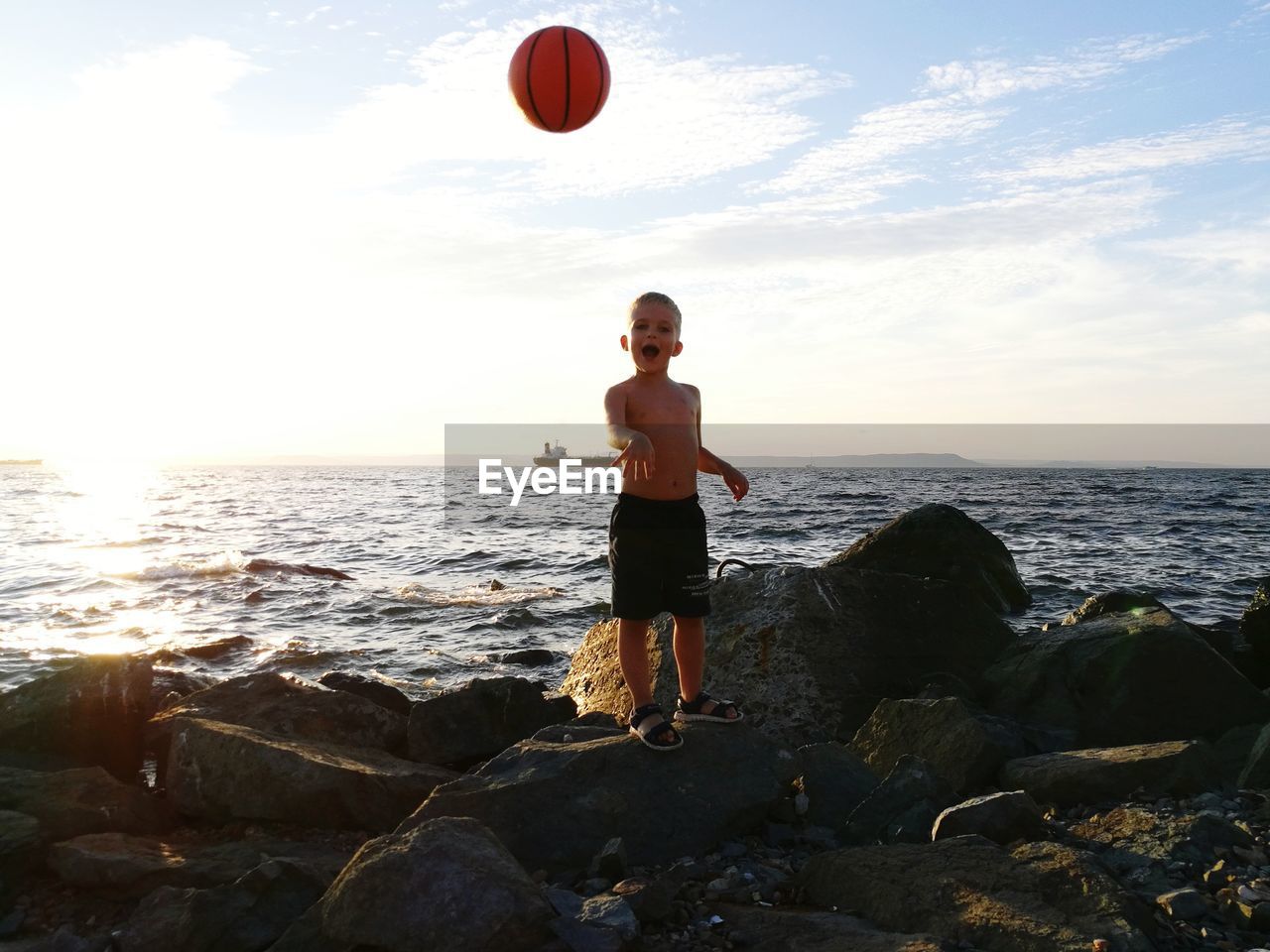 Full length of shirtless boy playing with ball at beach against sky