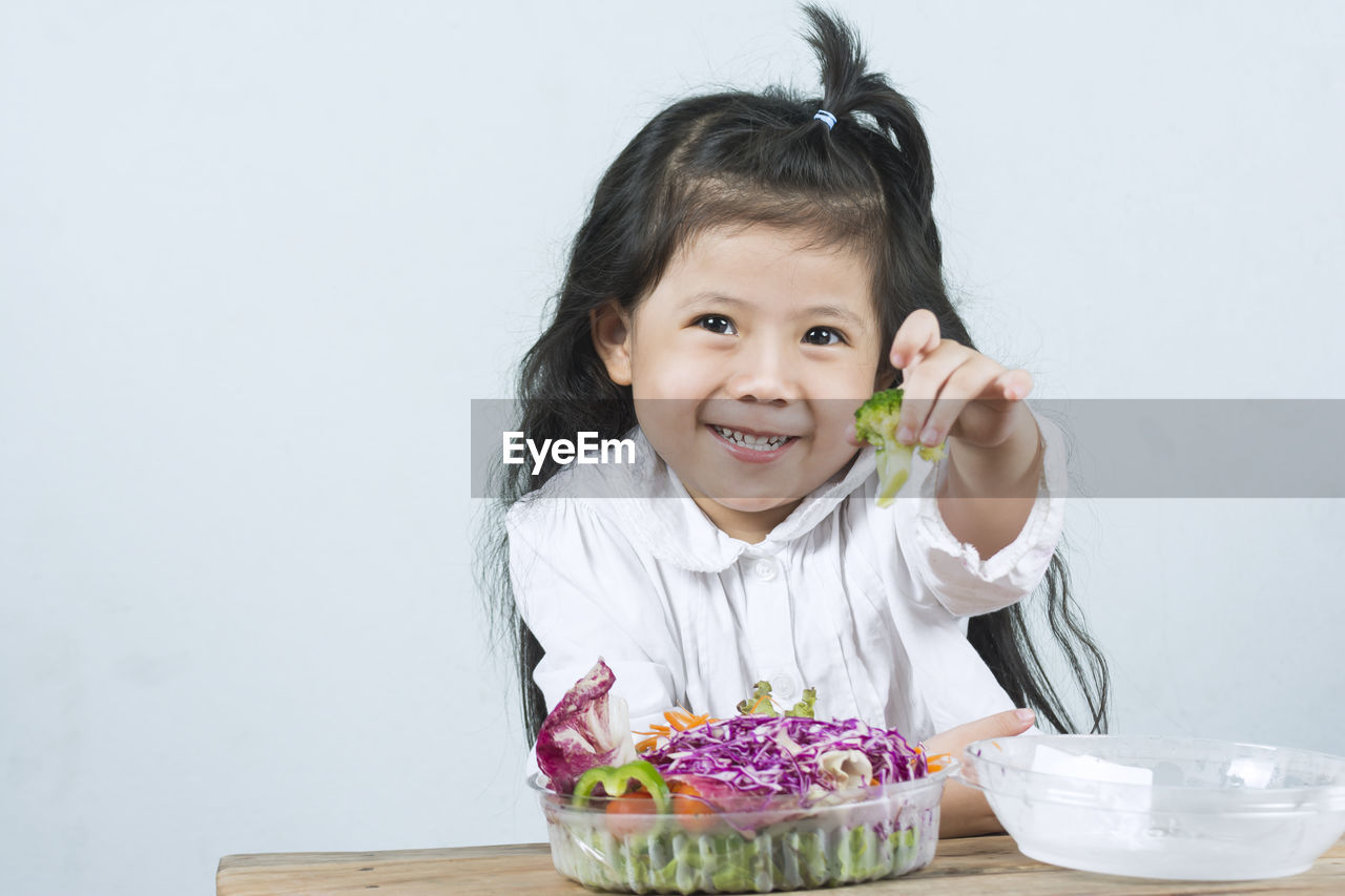 Portrait of smiling cute girl offering broccoli