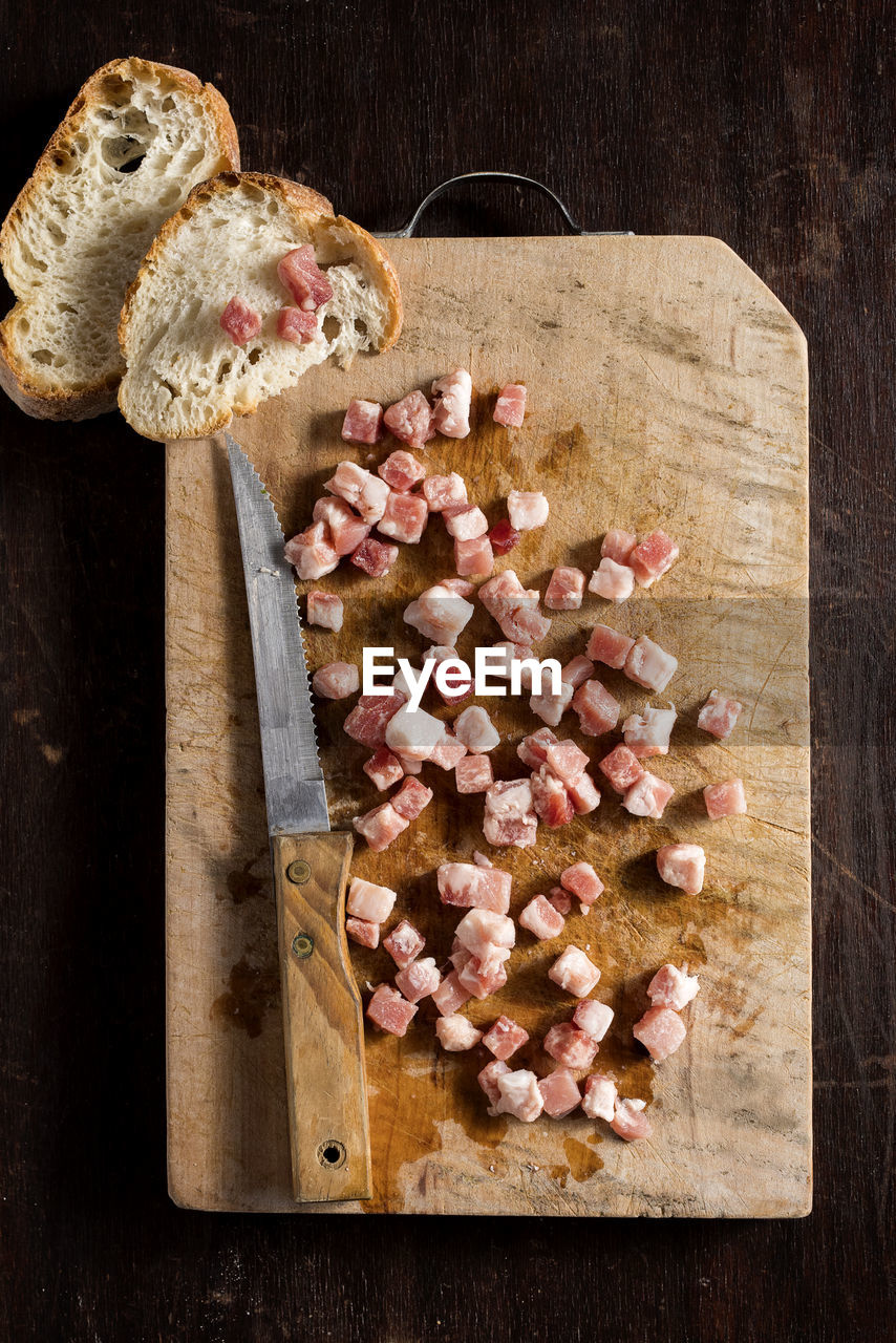 Little cubes of raw pancetta - bacon on a rustic wooden cutting board. top view. copy space.