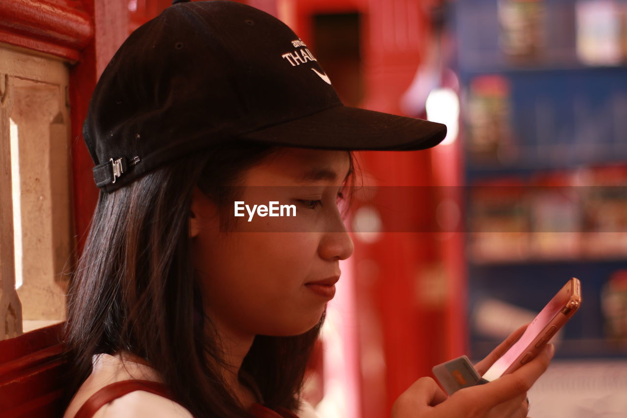 Side view of young woman wearing cap while using mobile phone