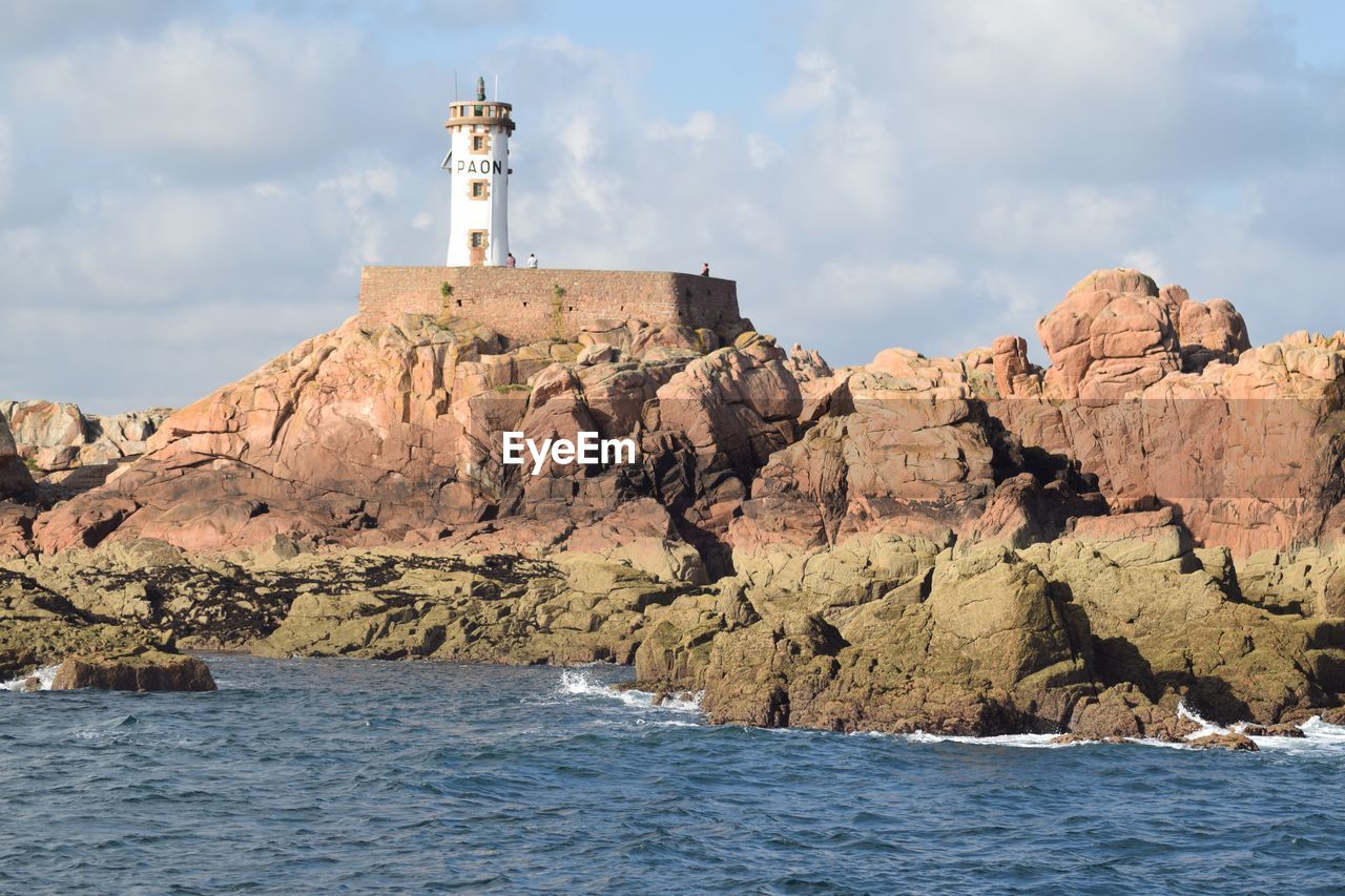 Lighthouse on rock by sea against sky