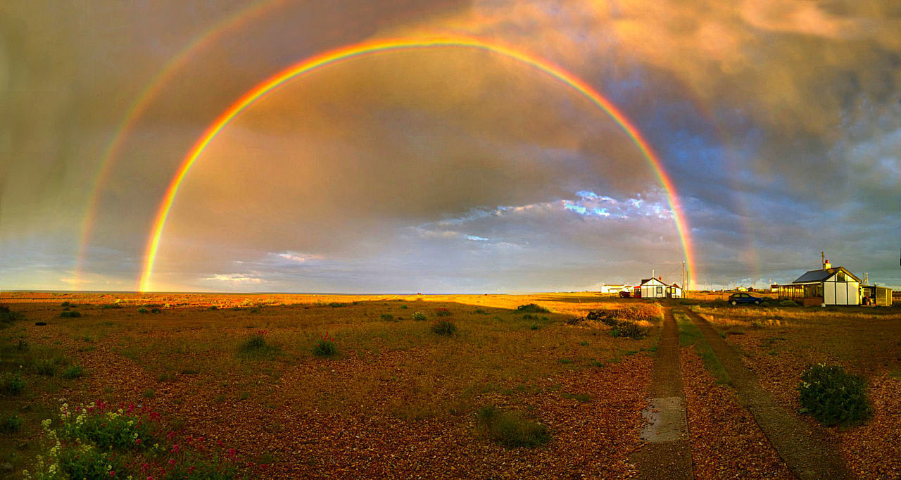 Double rainbows over landscape against cloudy sky during sunset