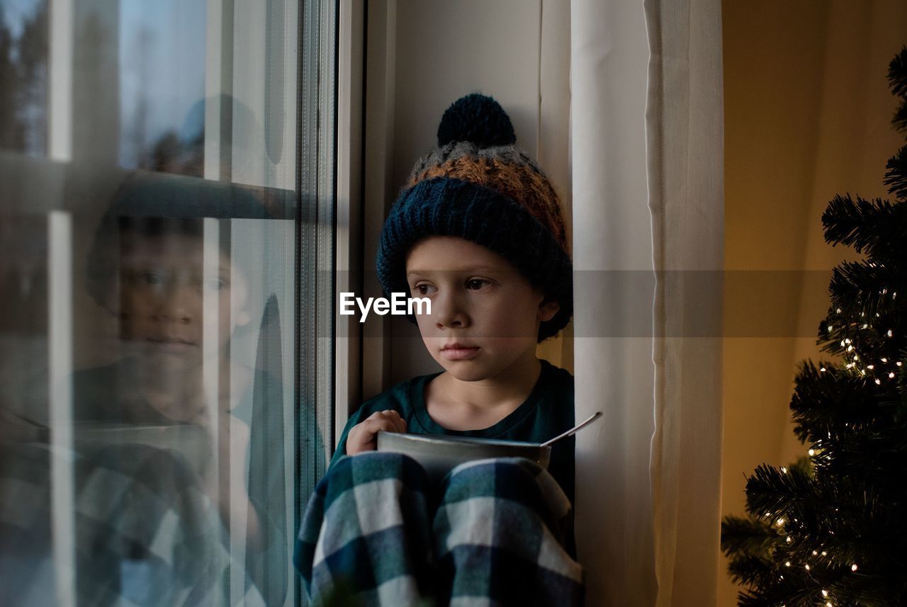 Young boy holding a cereal bowl looking out the window at christmas