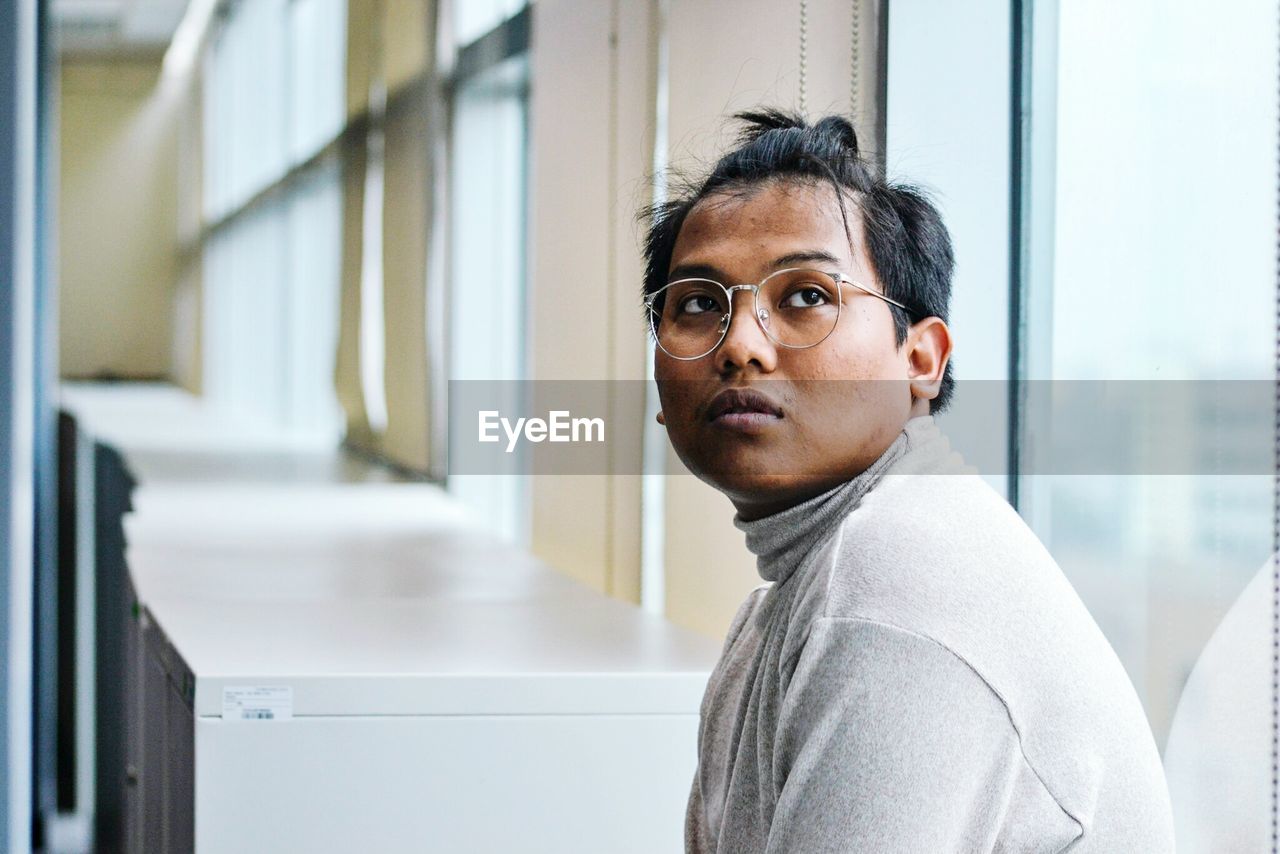 Side view of man looking away while sitting by window