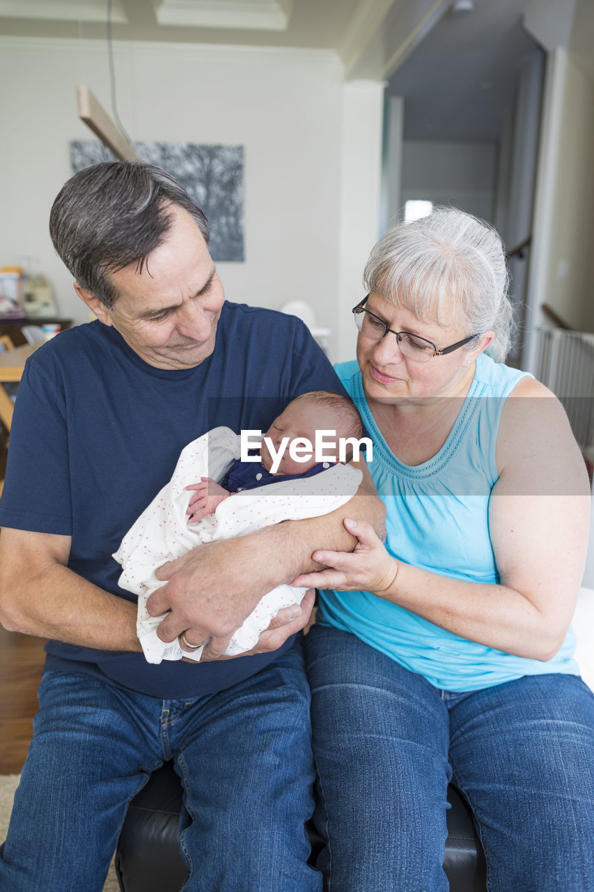 Grandparents with cute newborn granddaughter sitting at home