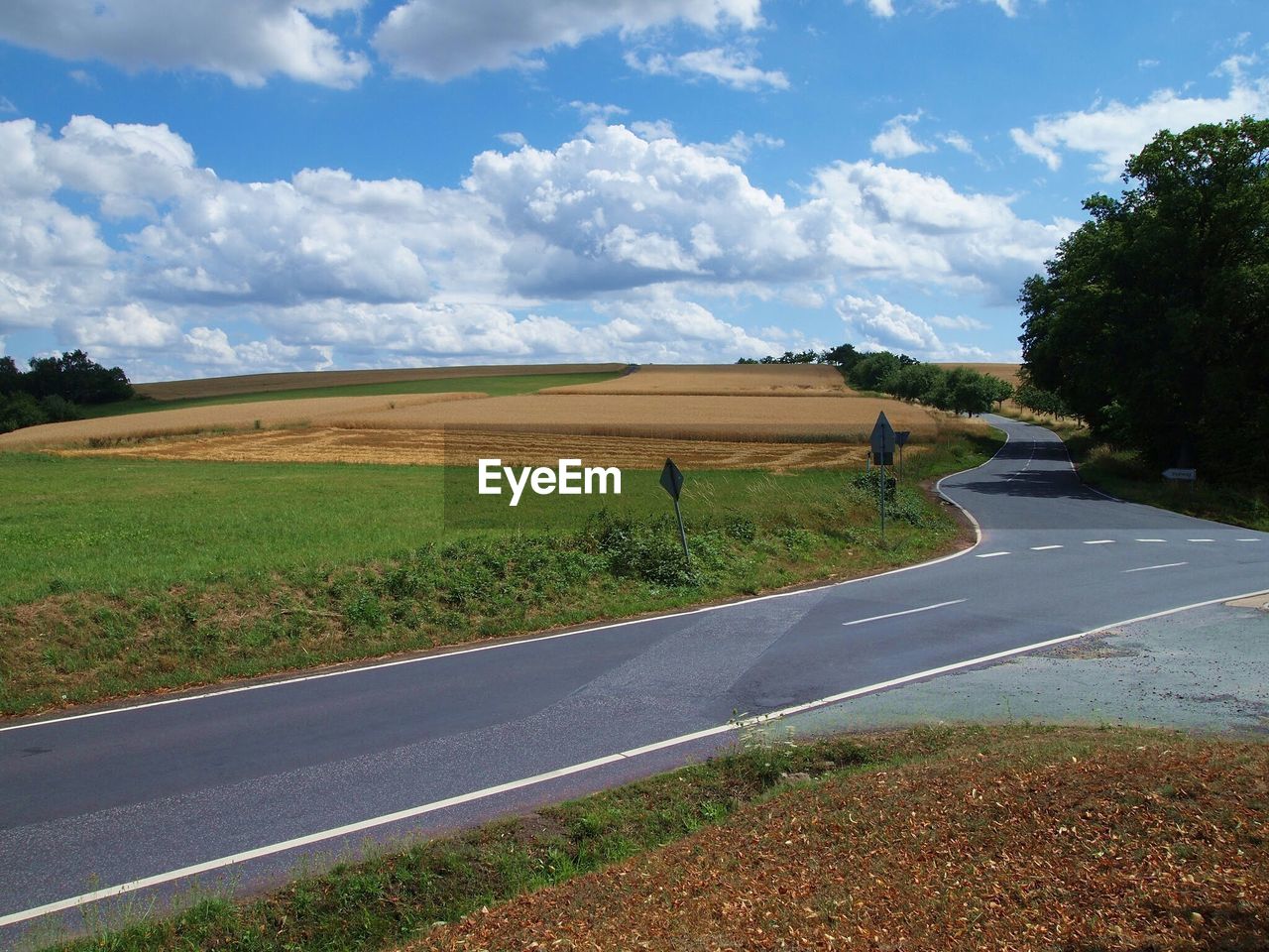 Country road by agricultural field against cloudy sky