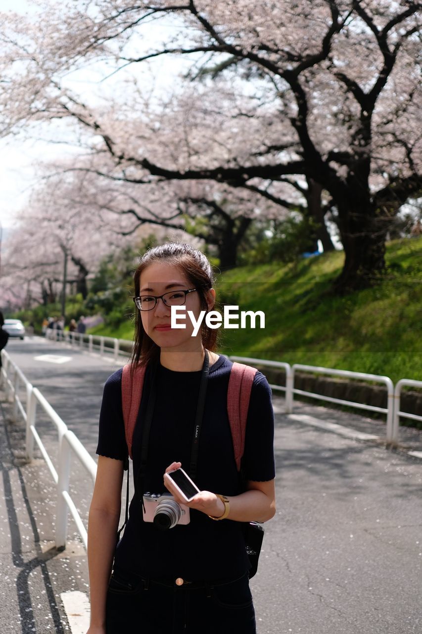 Young woman using phone while standing on tree