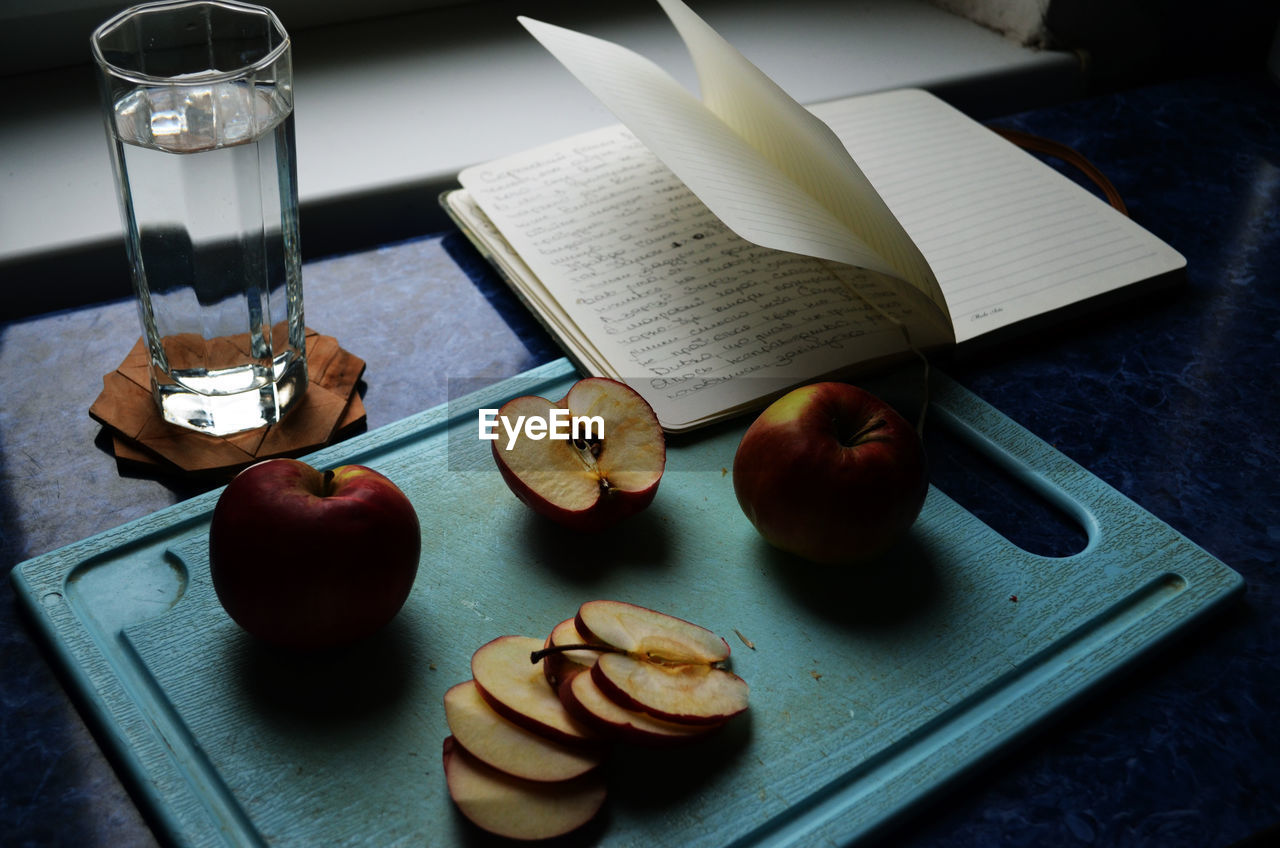 Directly above shot of apple slices with textbook and drinking water on table