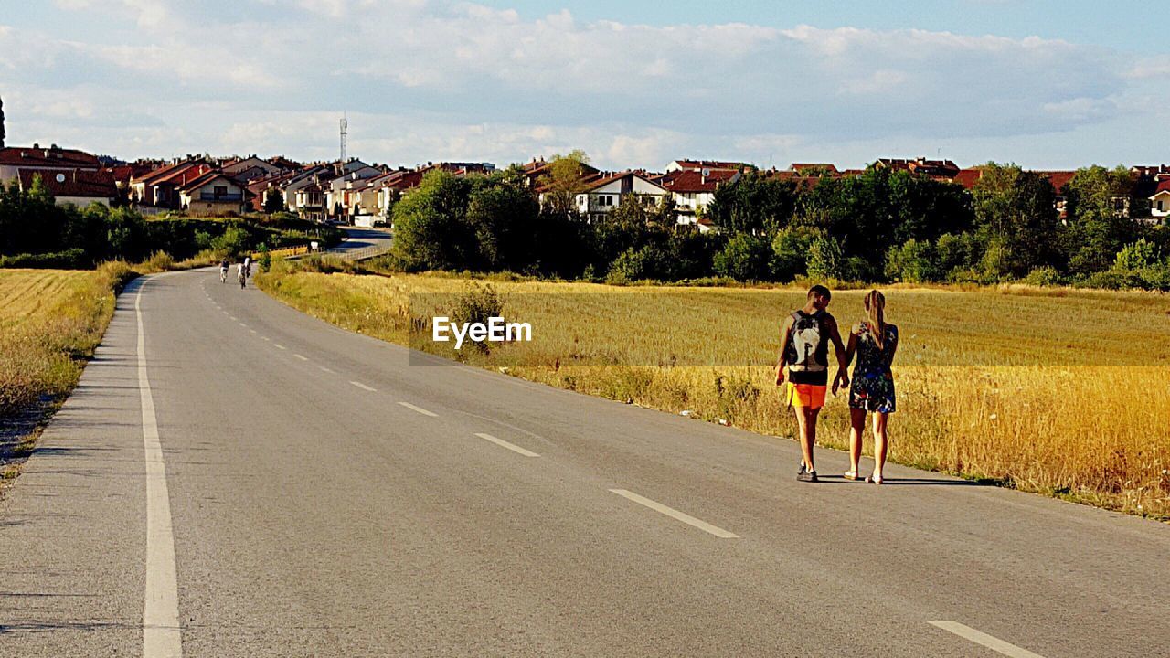 REAR VIEW OF PEOPLE RIDING ON ROAD