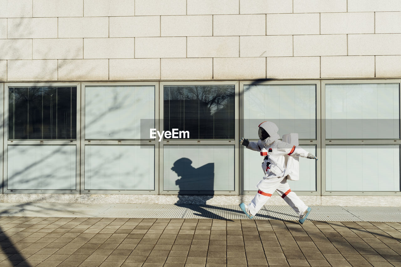 Female astronaut walking at building in city during sunny day