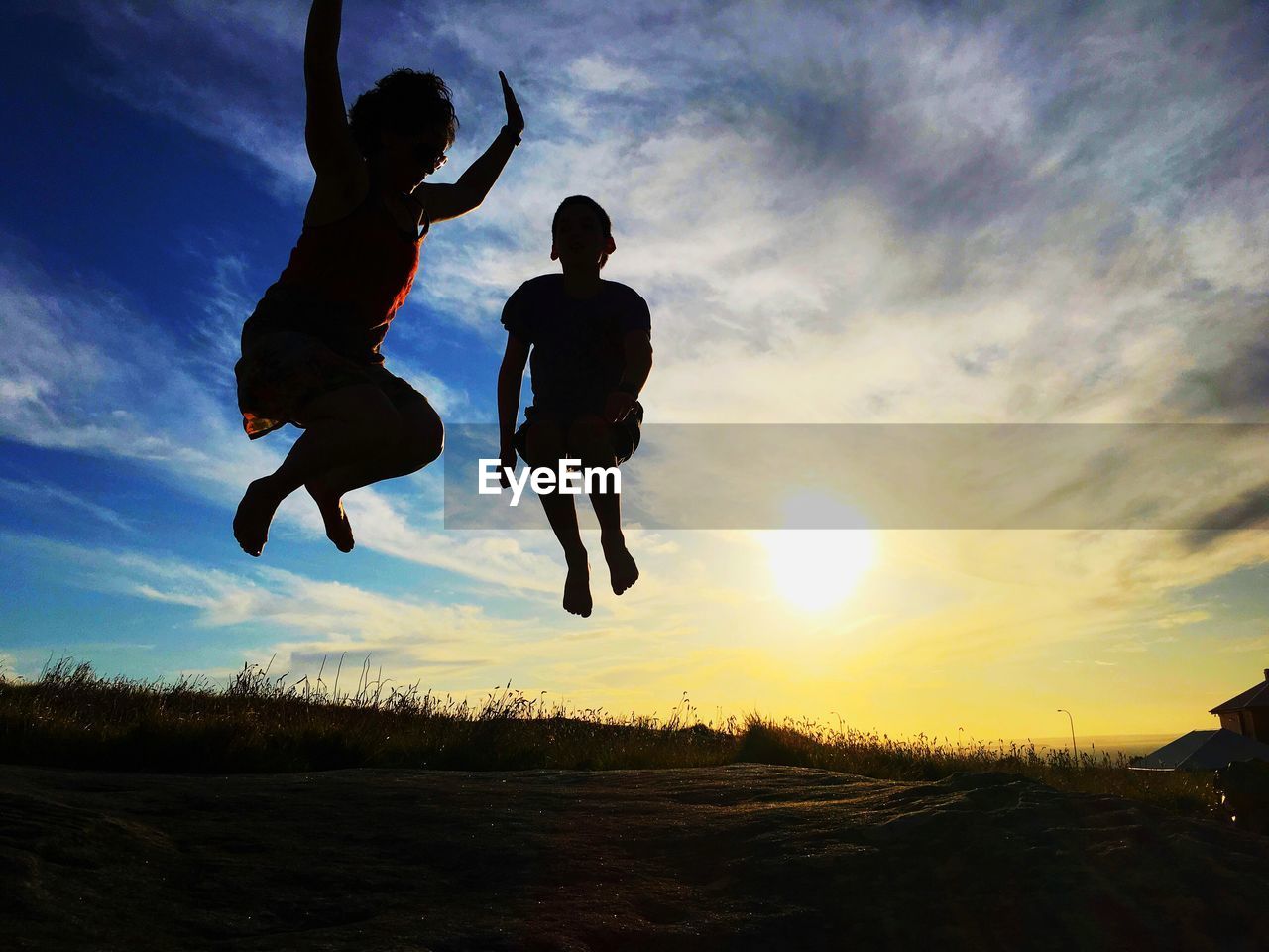 Full length of playful silhouette mother with son jumping over field against sky during sunset