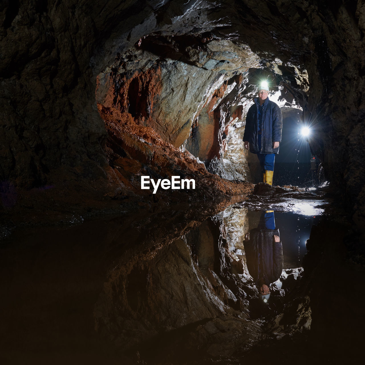 Man with illuminated headlamp standing in cave