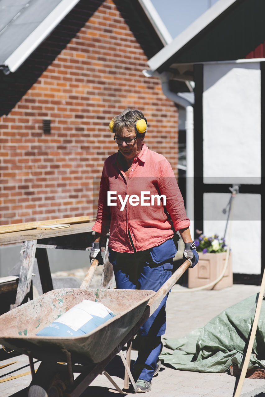 Senior woman pushing wheelbarrow at yard outside house