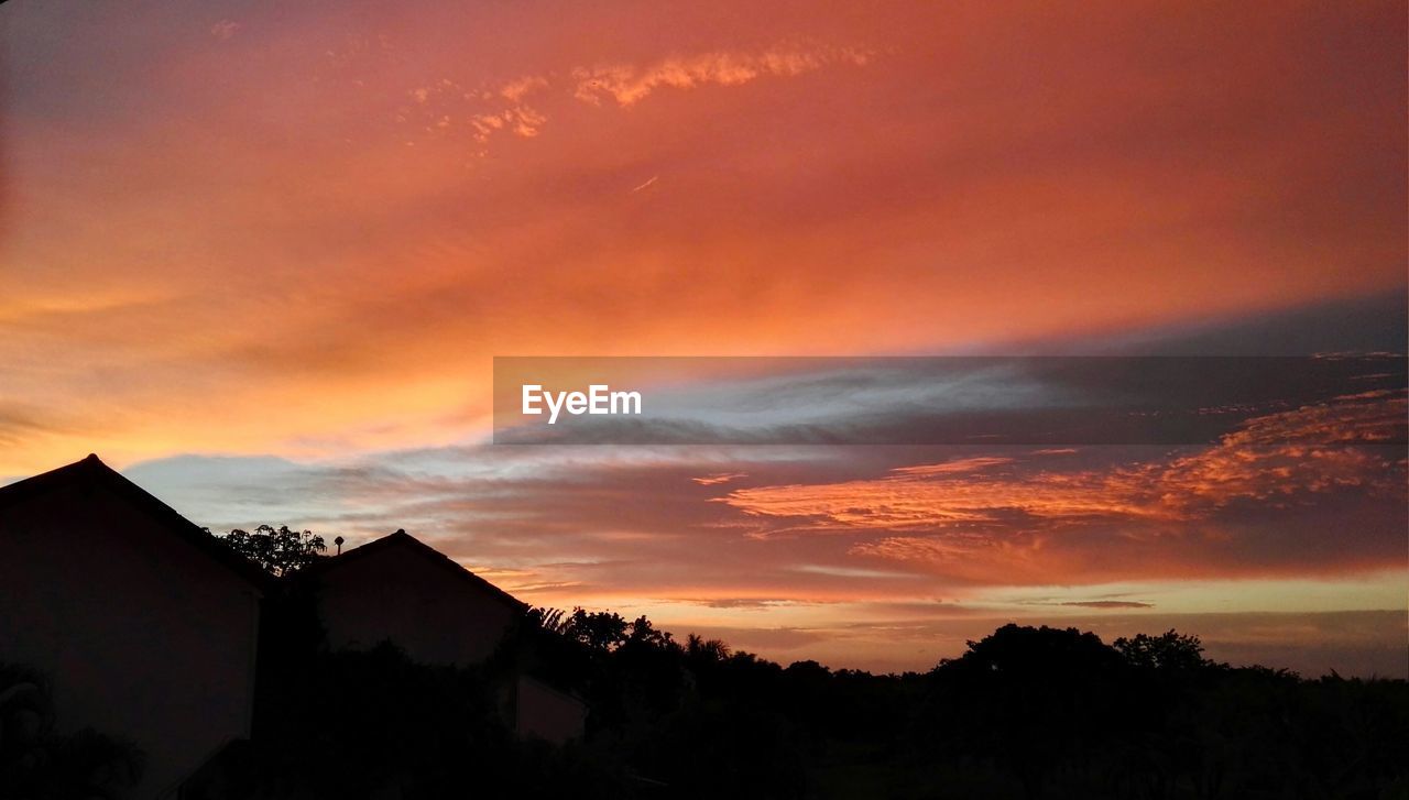 Silhouette mountain and trees against cloudy sky during sunset