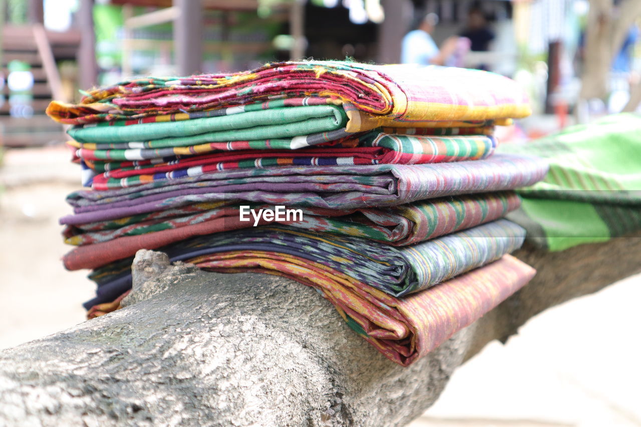 Close-up of multi colored textiles over fallen tree for sale at market stall