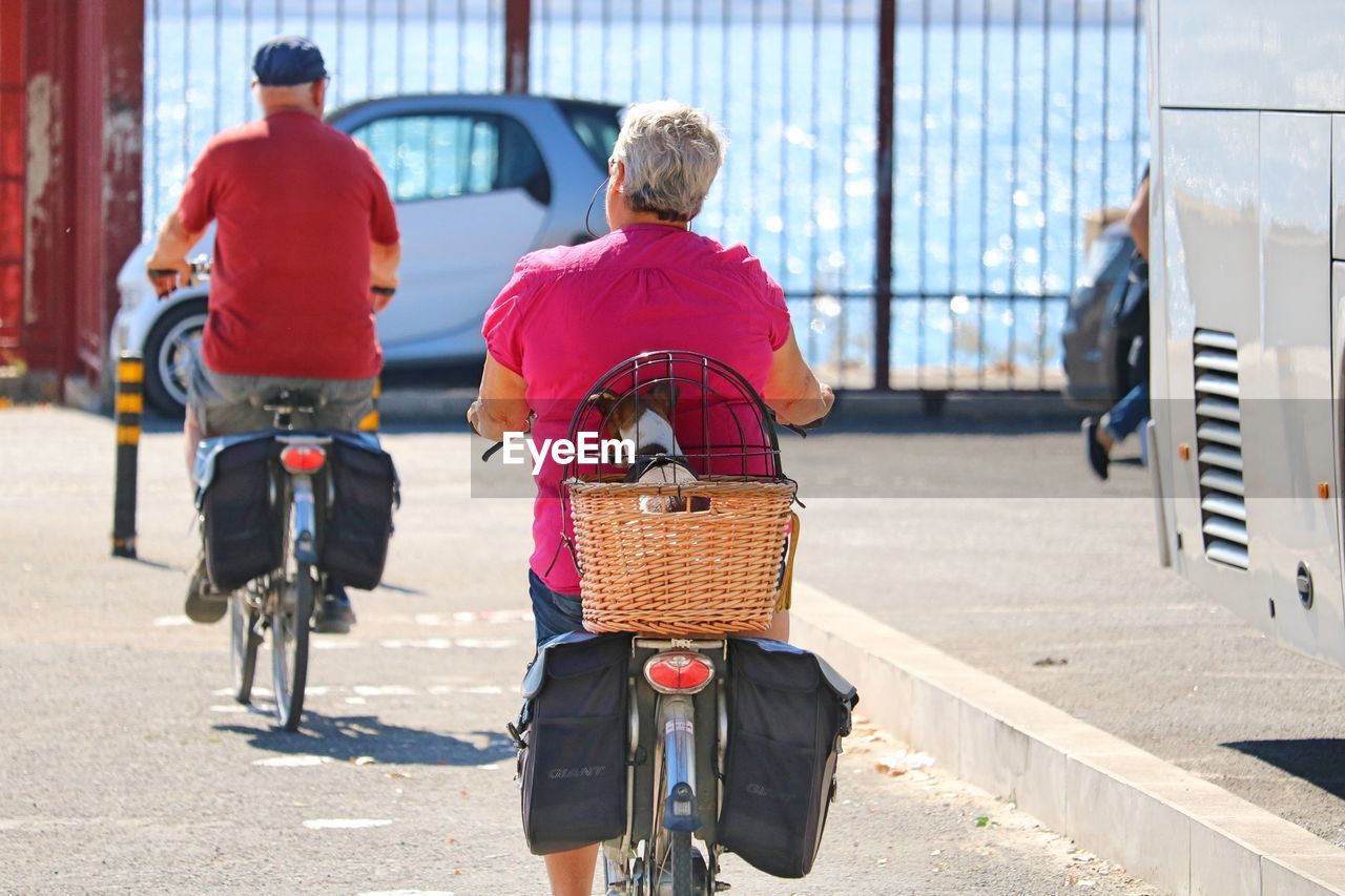 REAR VIEW OF MEN RIDING BICYCLE ON STREET IN CITY