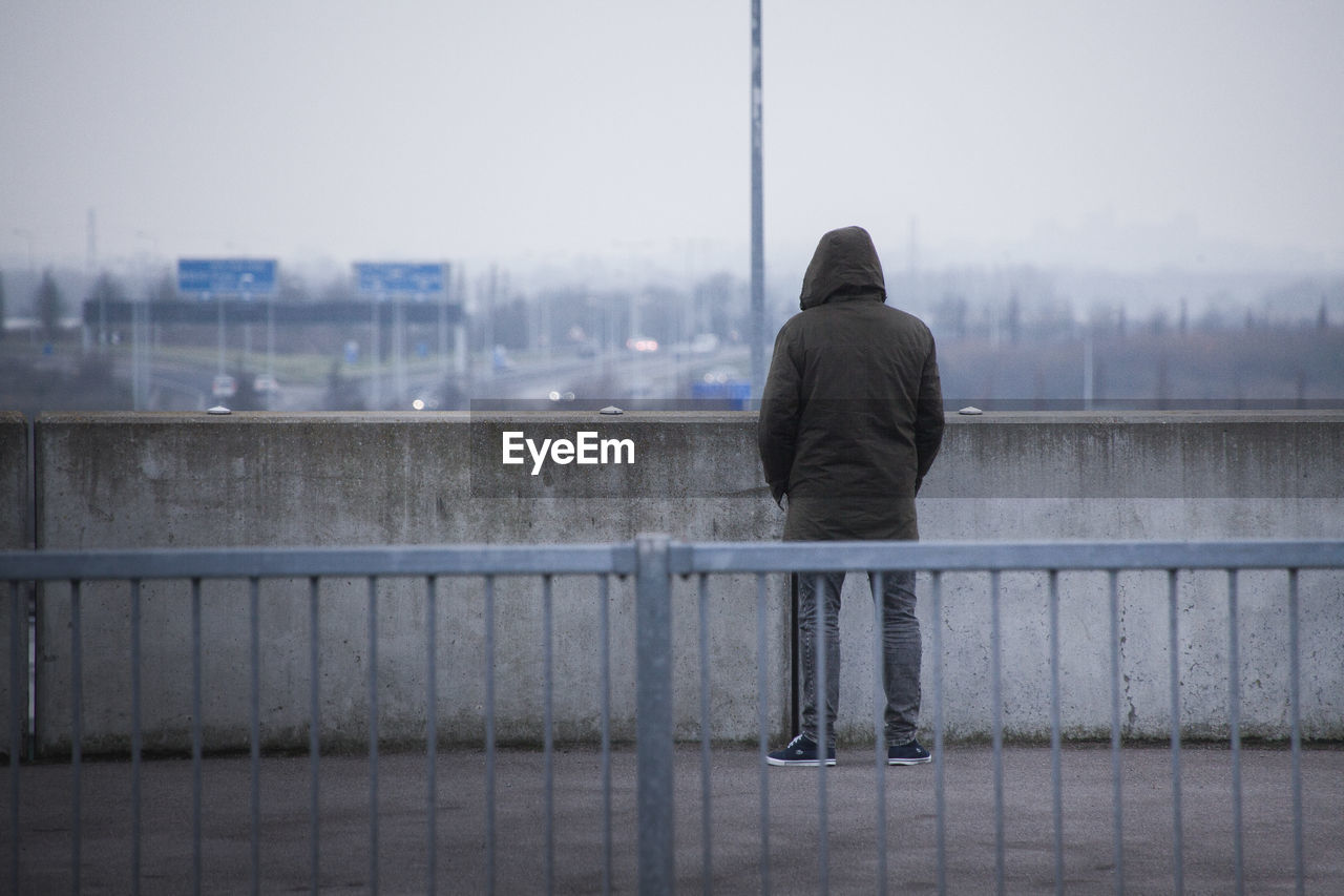 Rear view of man on railing by river in city