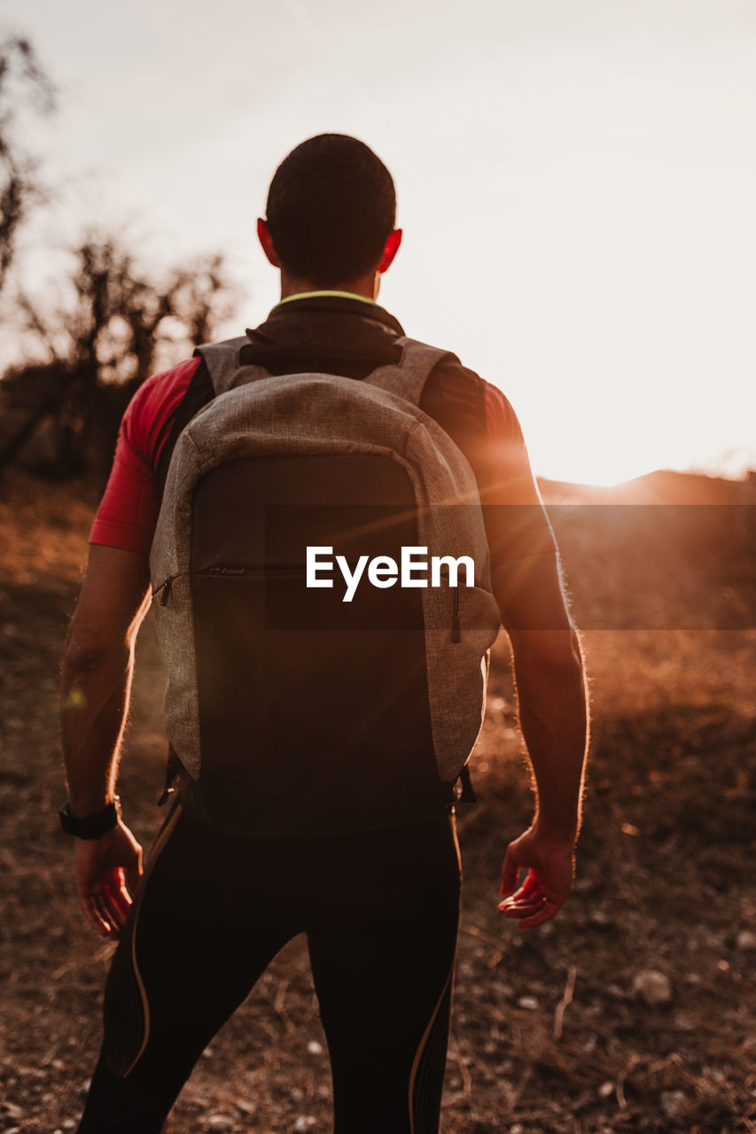 Rear view of man with backpack standing on field during sunset