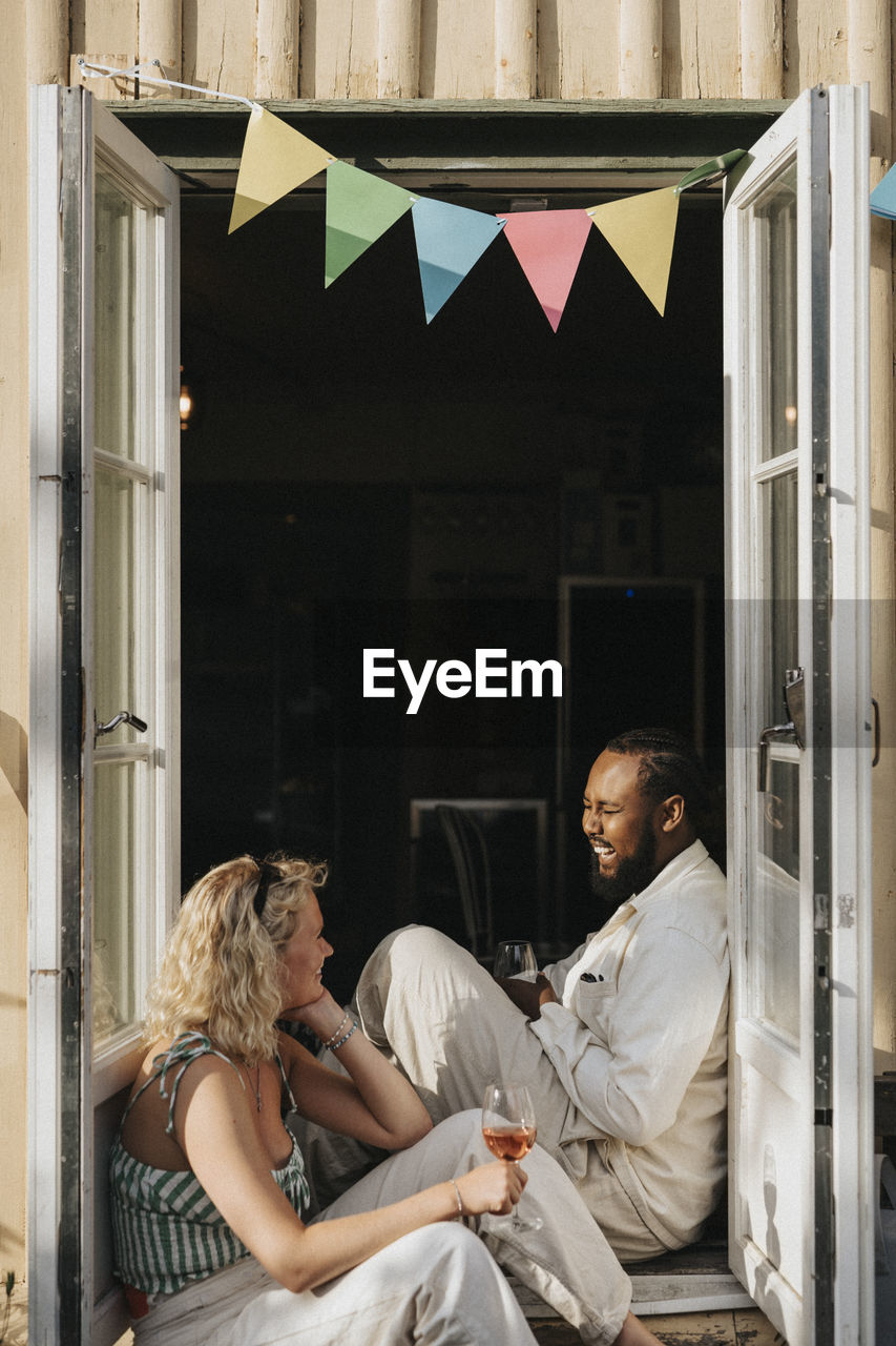 Happy male and female friends enjoying together while sitting at cafe doorway