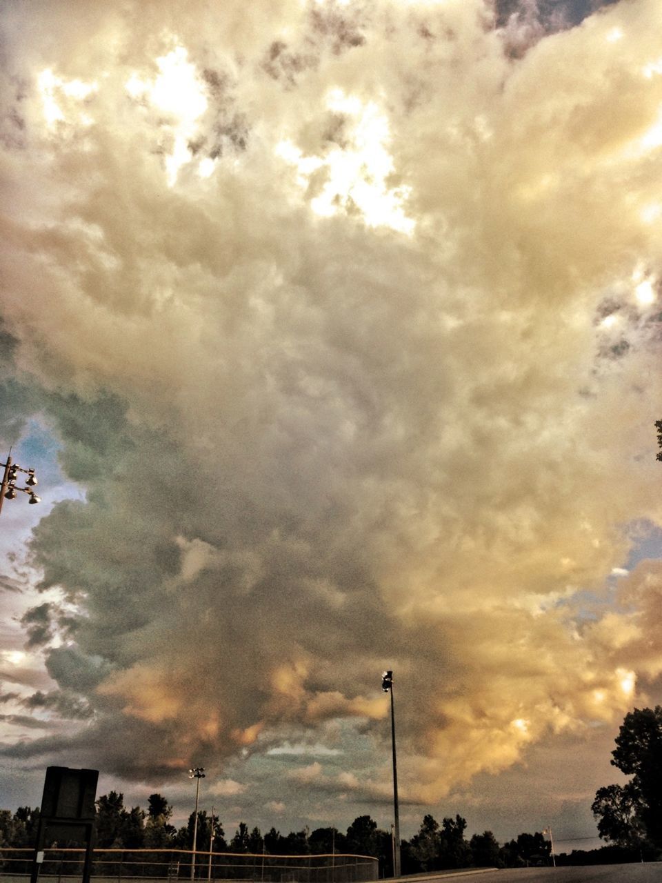 Low angle view of cloudy sky over street light and trees