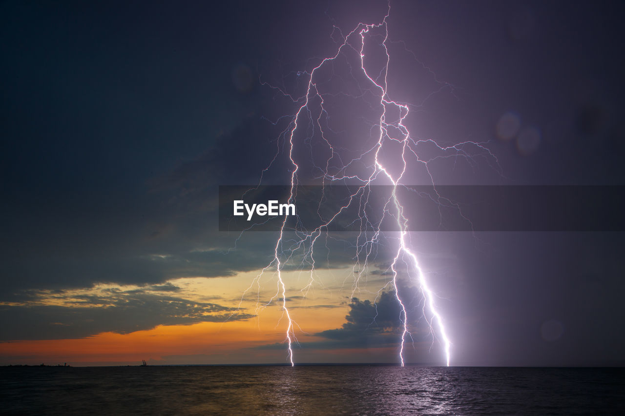 Forked lightning over sea against sky during sunset