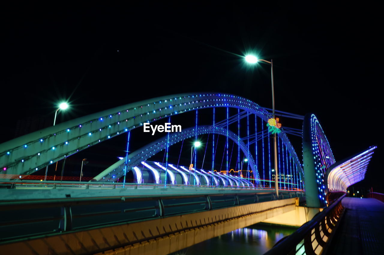 LOW ANGLE VIEW OF ILLUMINATED BRIDGE OVER RIVER AGAINST SKY