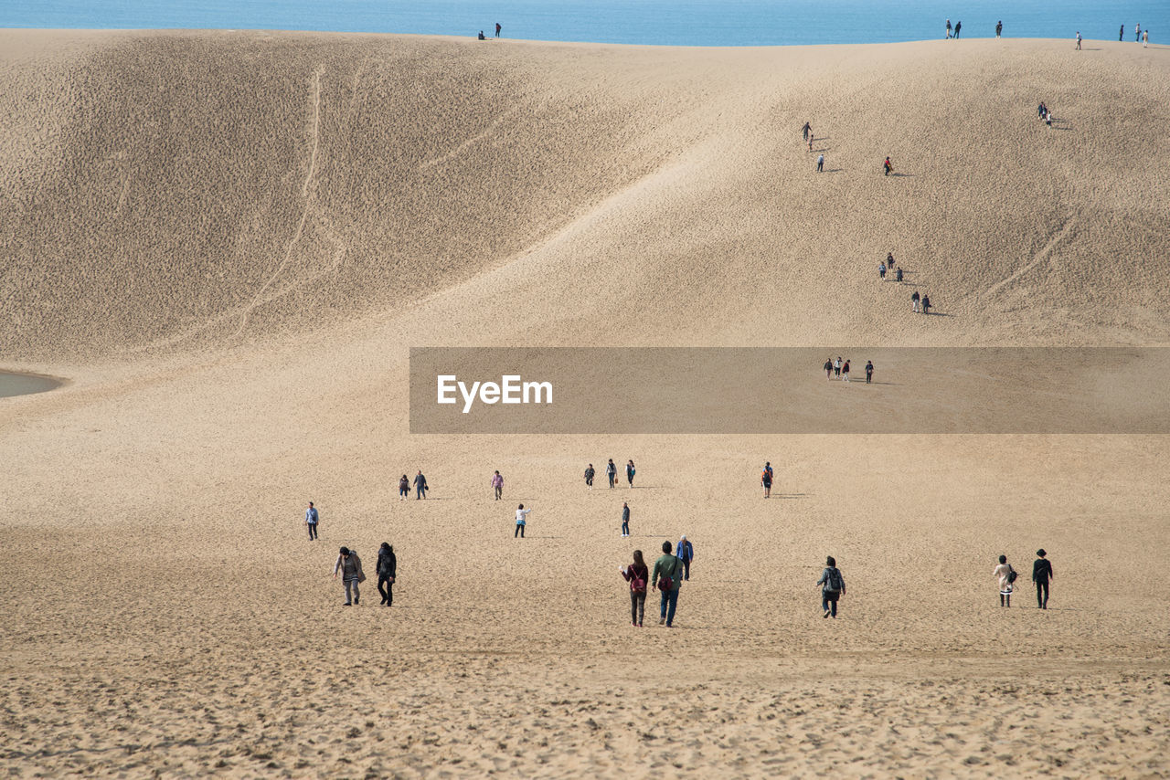 People on sand dune against clear sky