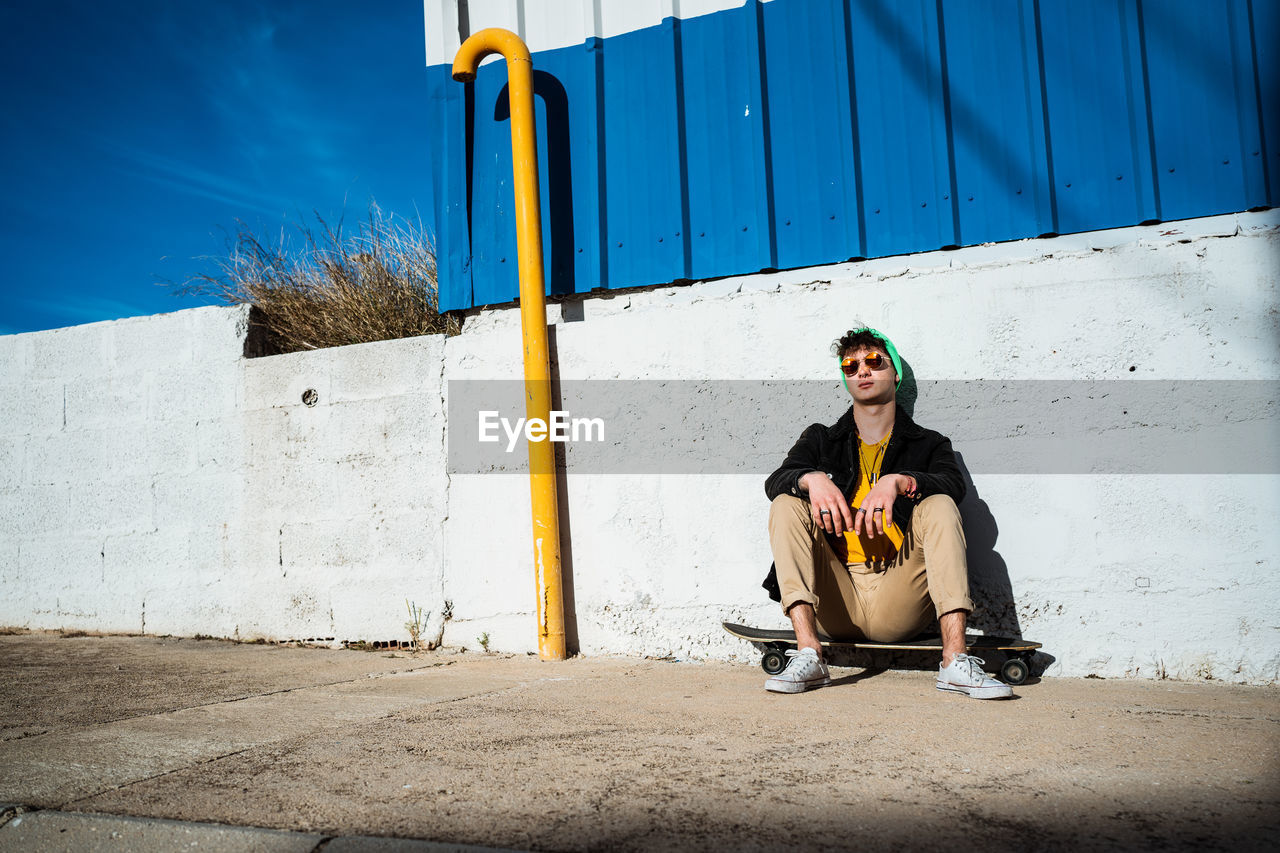 PORTRAIT OF YOUNG MAN SITTING ON WALL