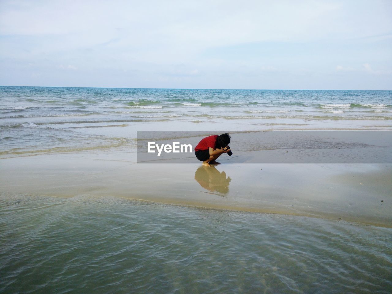 Woman photographing while crouching at sandbar