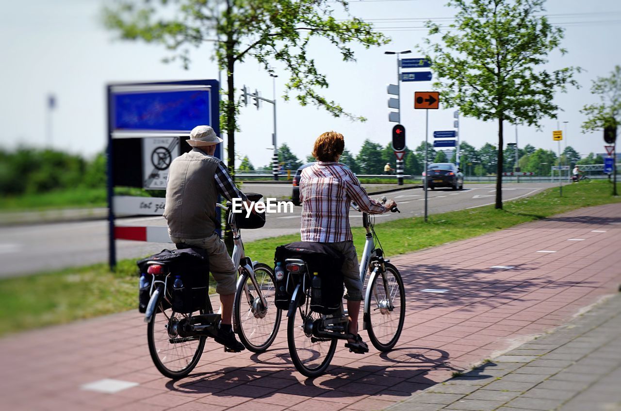 REAR VIEW OF MAN RIDING BICYCLE ON ROAD