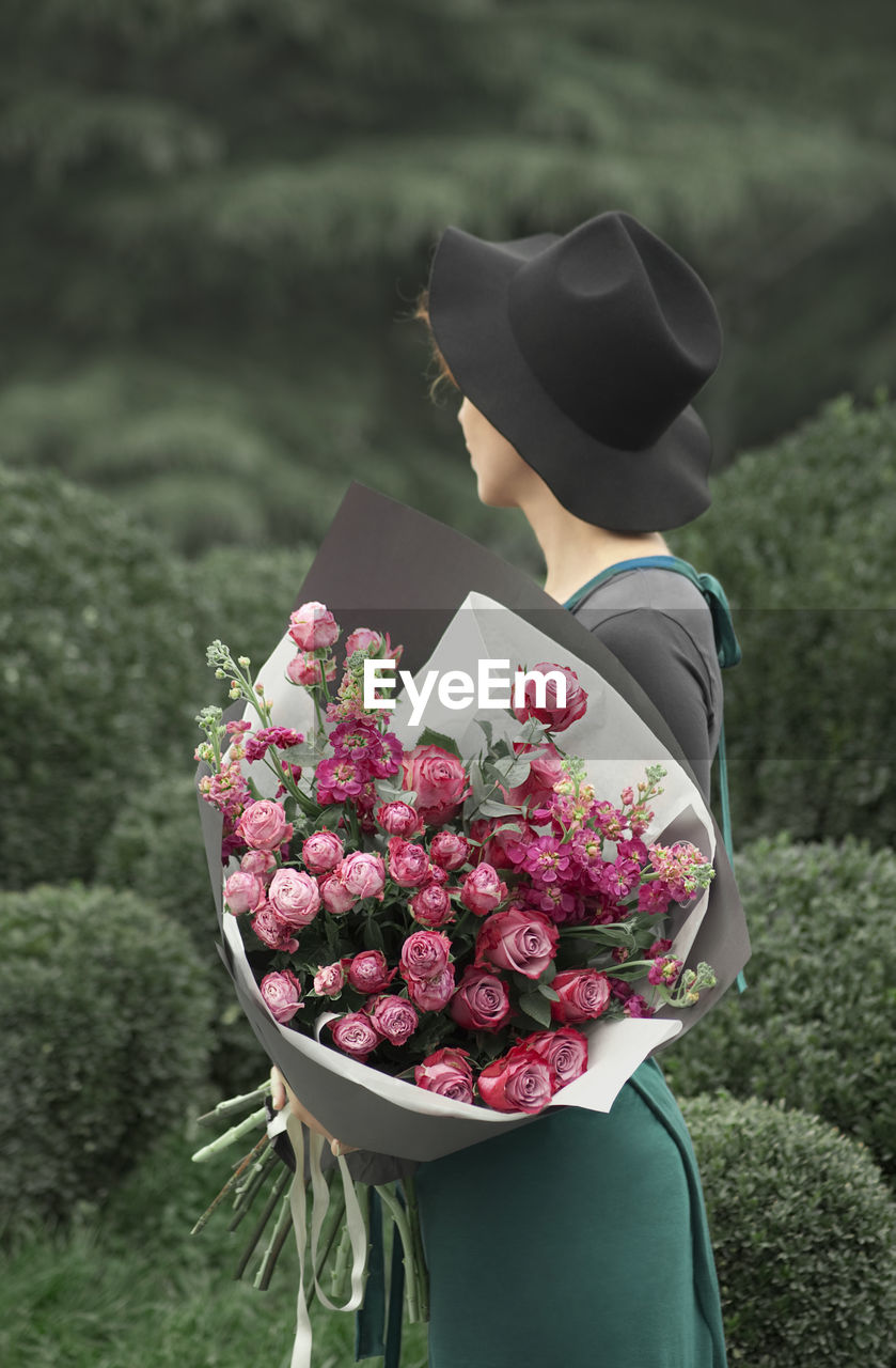 Young woman looking away while holding flower bouquet at outdoors