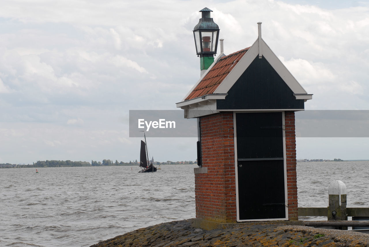 LIGHTHOUSE BY SEA AGAINST BUILDINGS