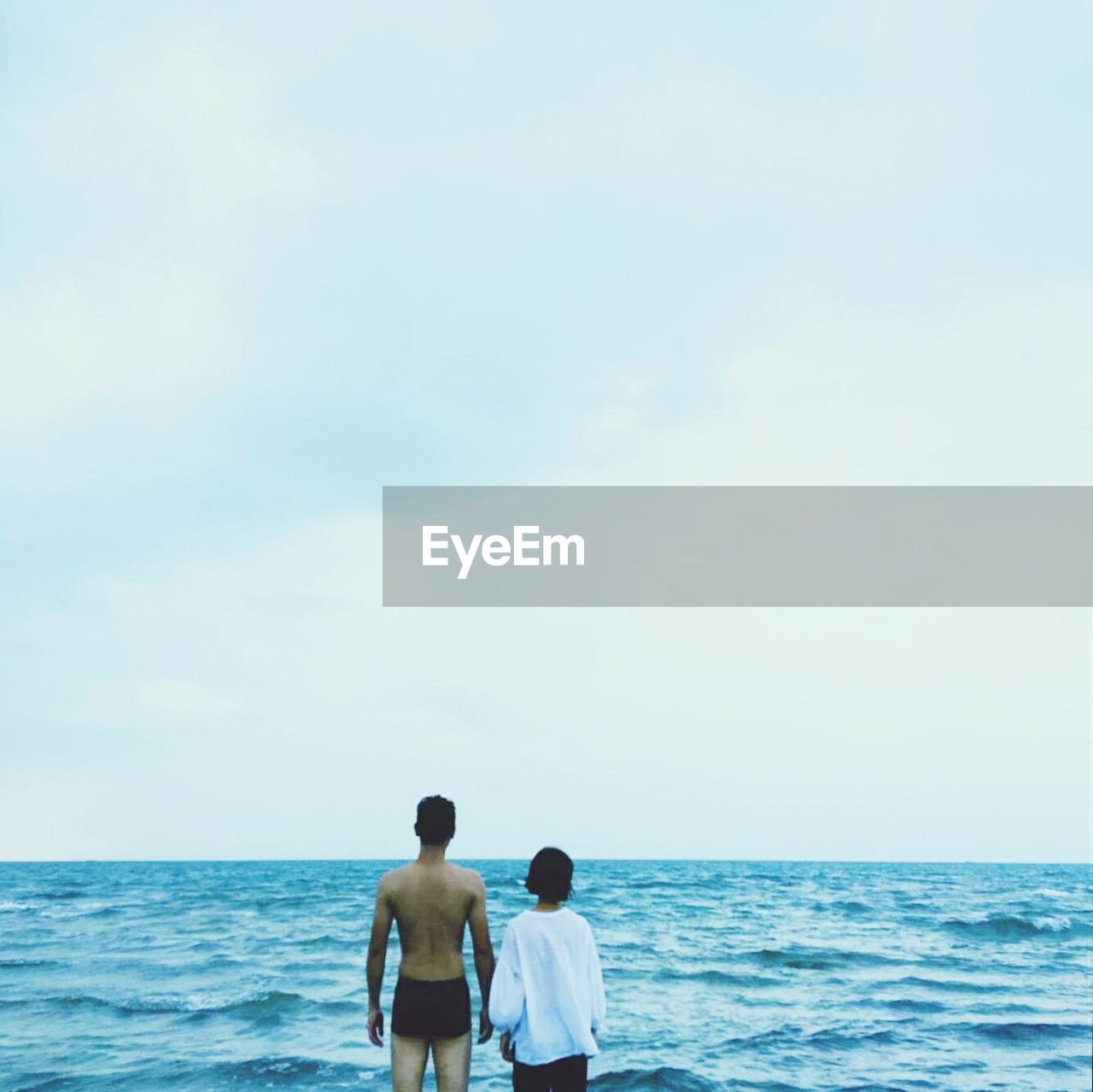 Rear view of couple standing on shore at beach against sky