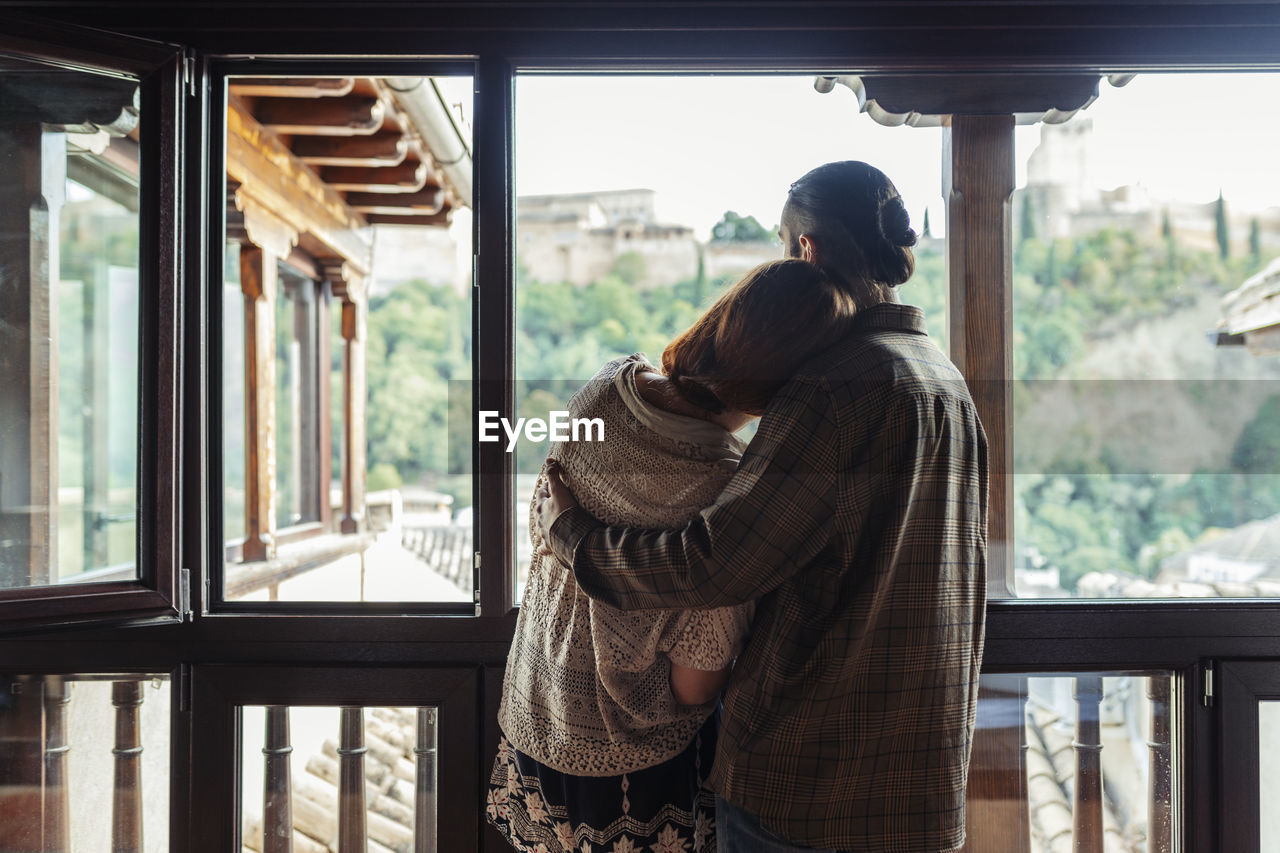 Couple with arm around standing by window at home